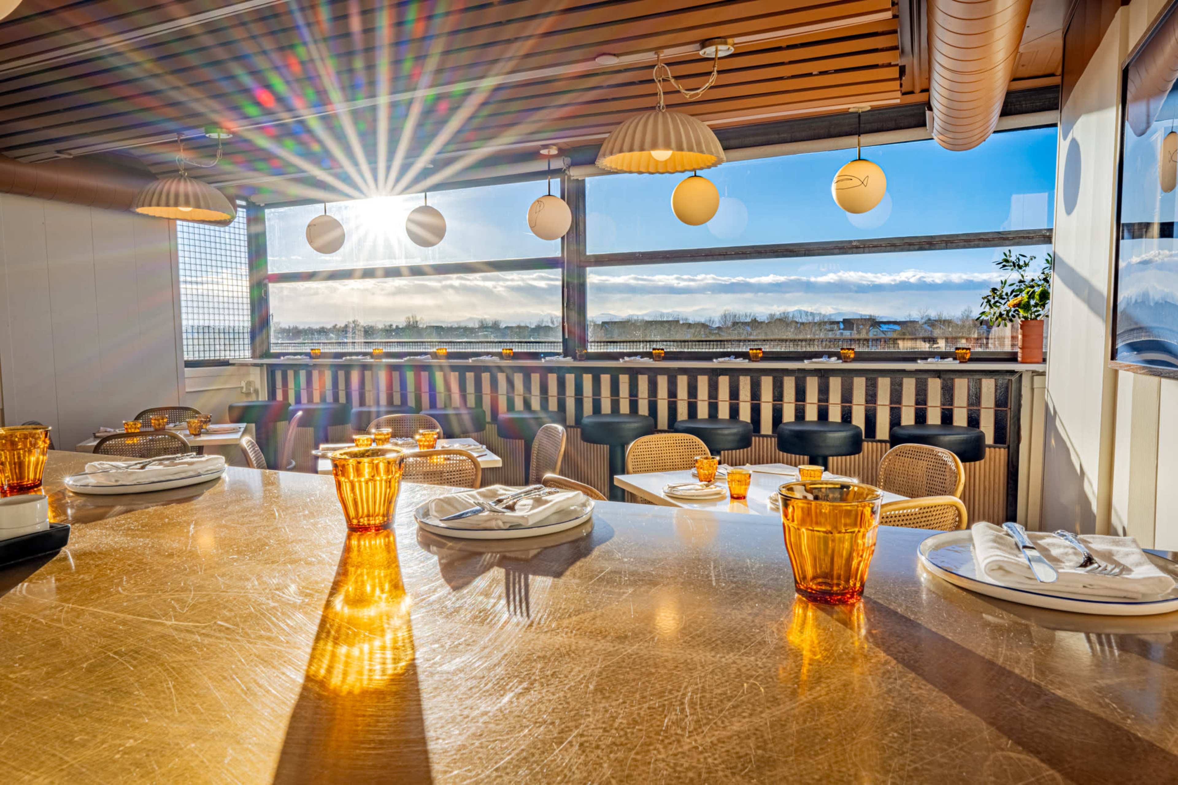 The image shows a brightly lit restaurant interior with tables set for dining and large windows letting in sunlight.