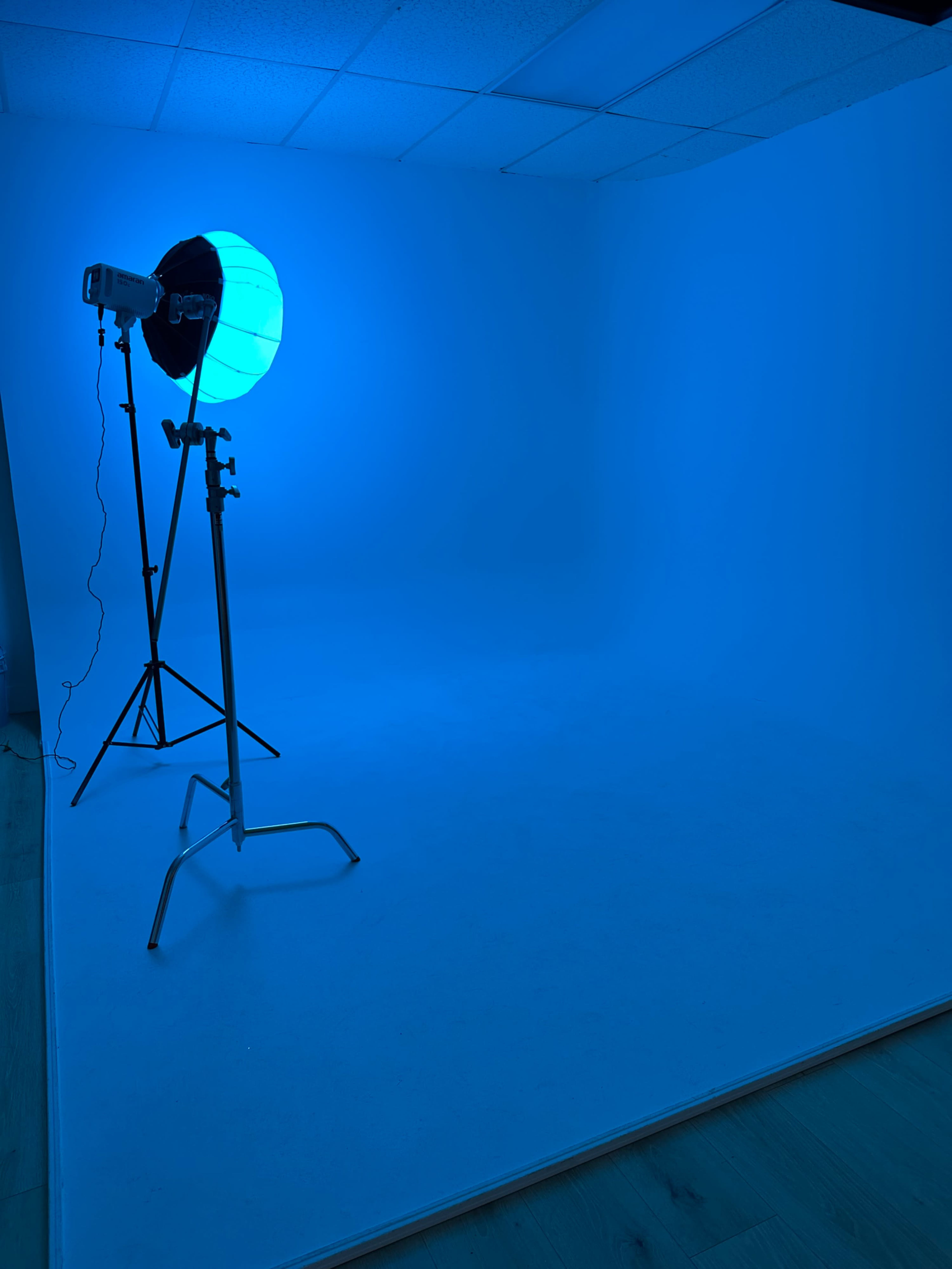The image shows a photography studio with a blue backdrop and an illuminated softbox light on a stand.