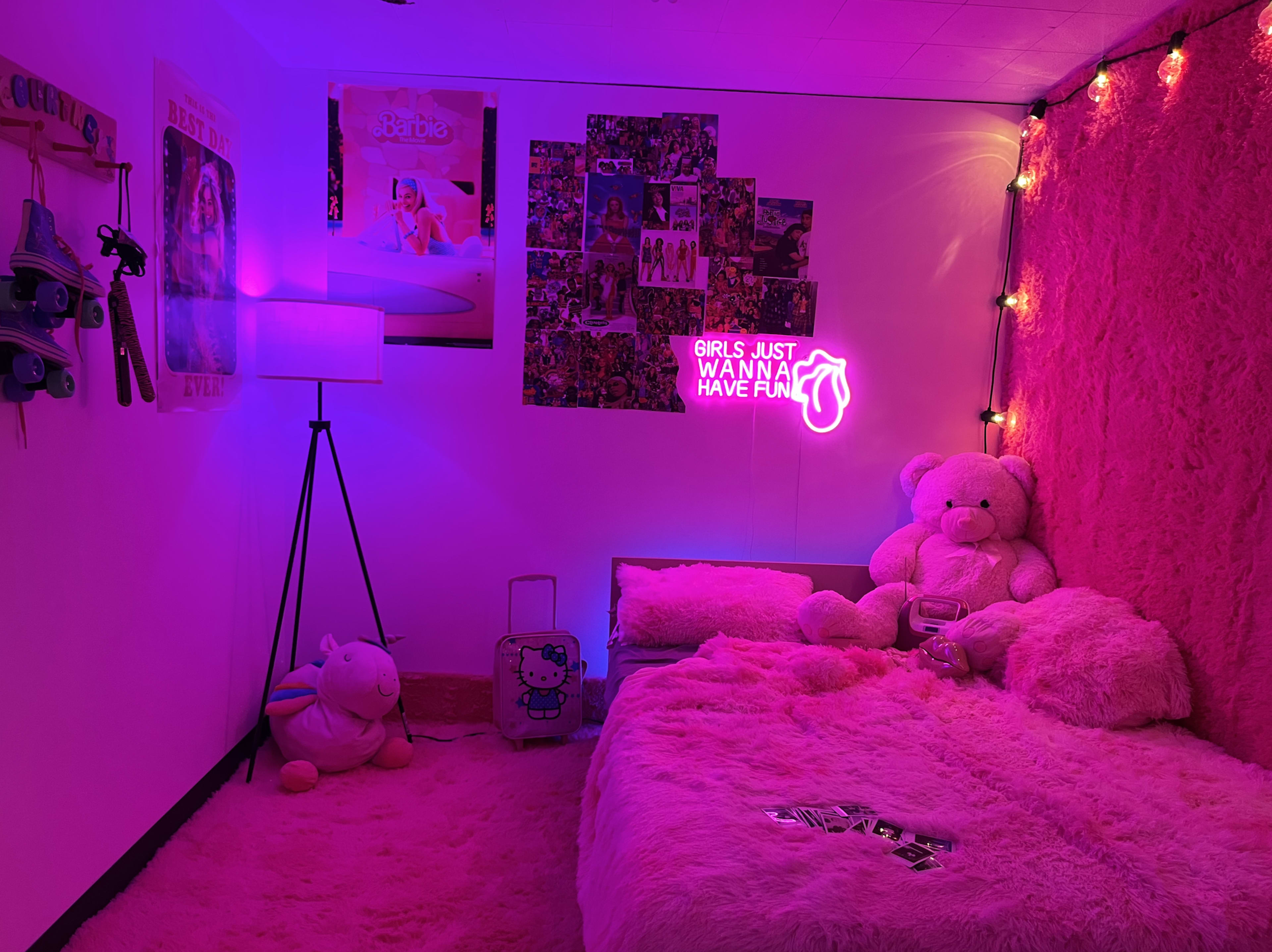 A brightly lit bedroom with pink walls, plush bedding, a floor covered in pink carpet, and a neon sign that reads "GIRLS JUST WANNA HAVE FUN."