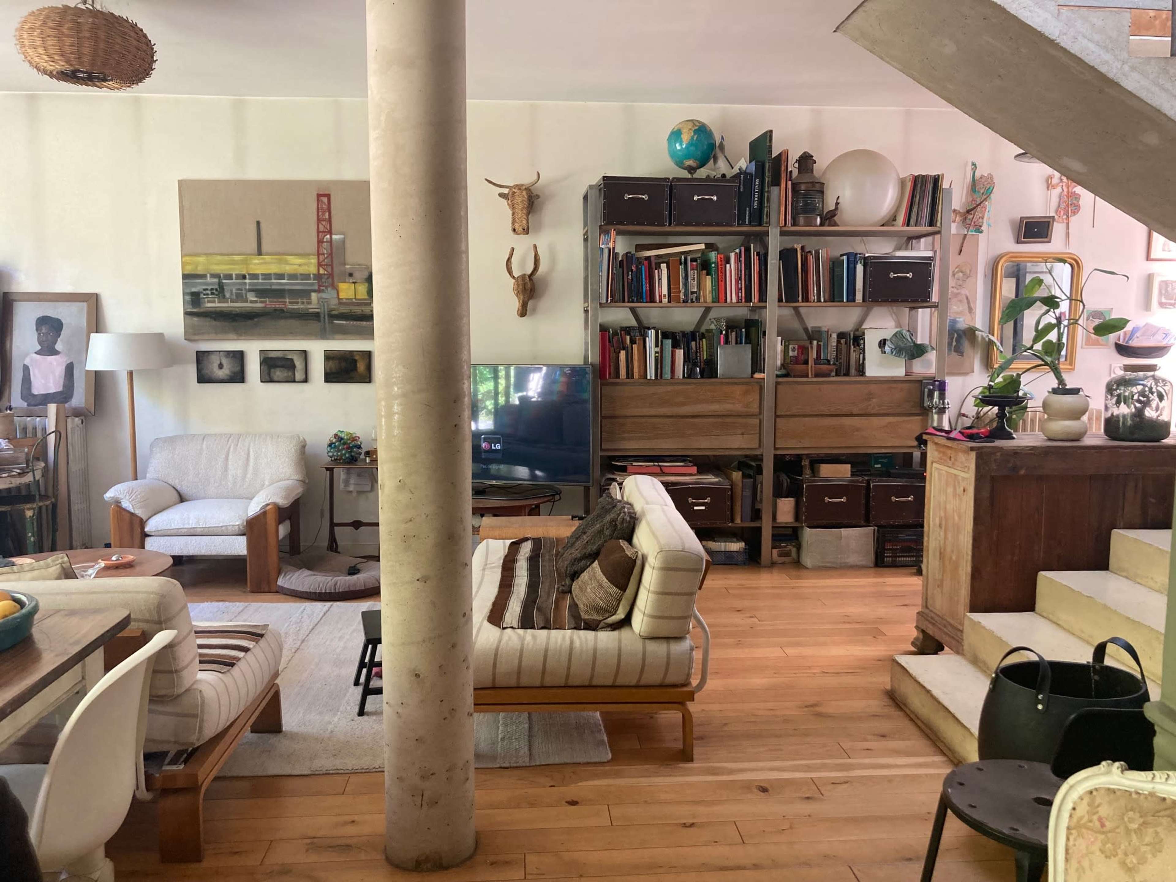 The image shows a living room with a mix of modern and vintage furniture, bookshelves filled with books, and various decorative items on display.