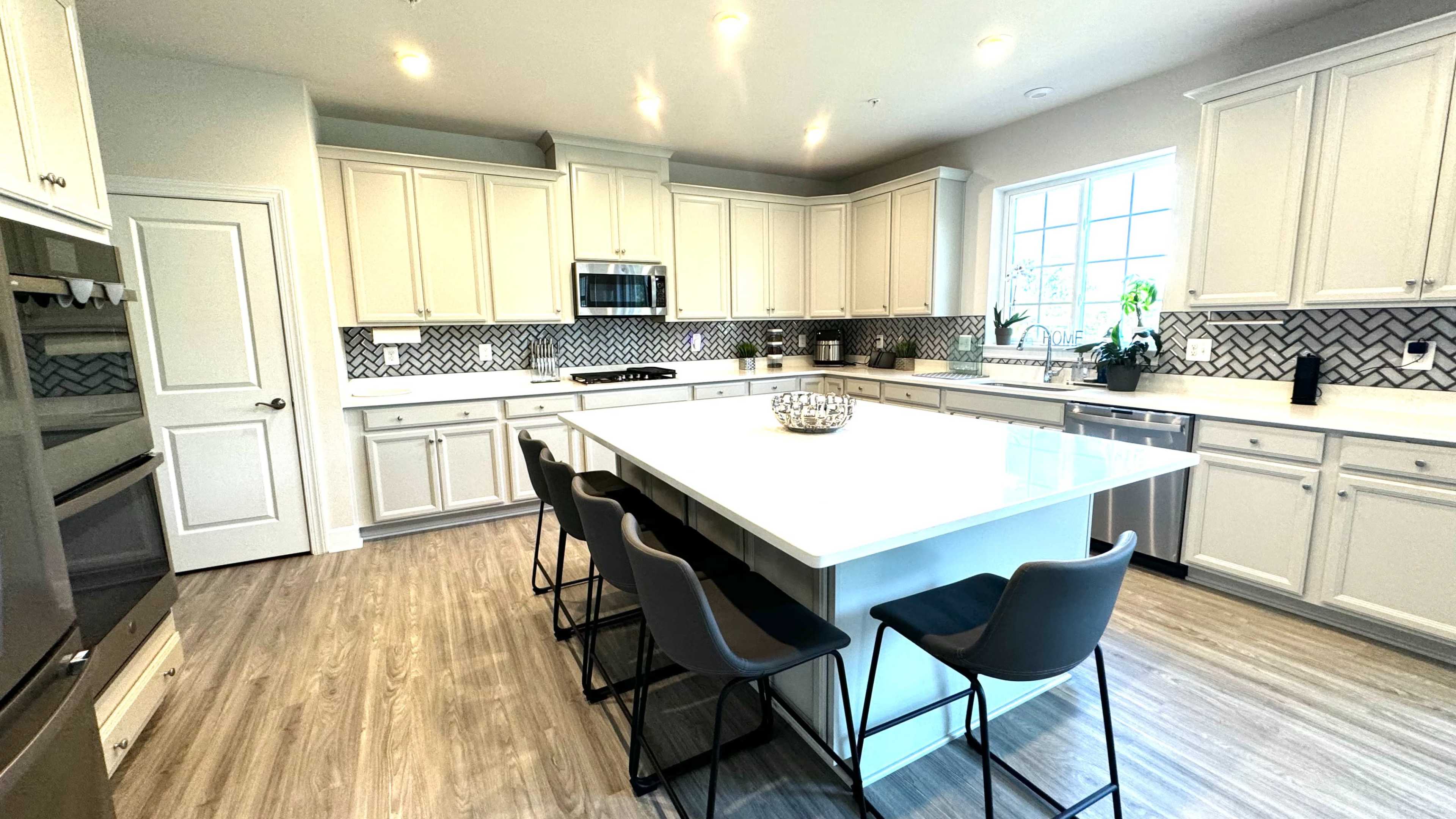 A modern kitchen with white cabinets, a large island with seating, and a herringbone-patterned backsplash.