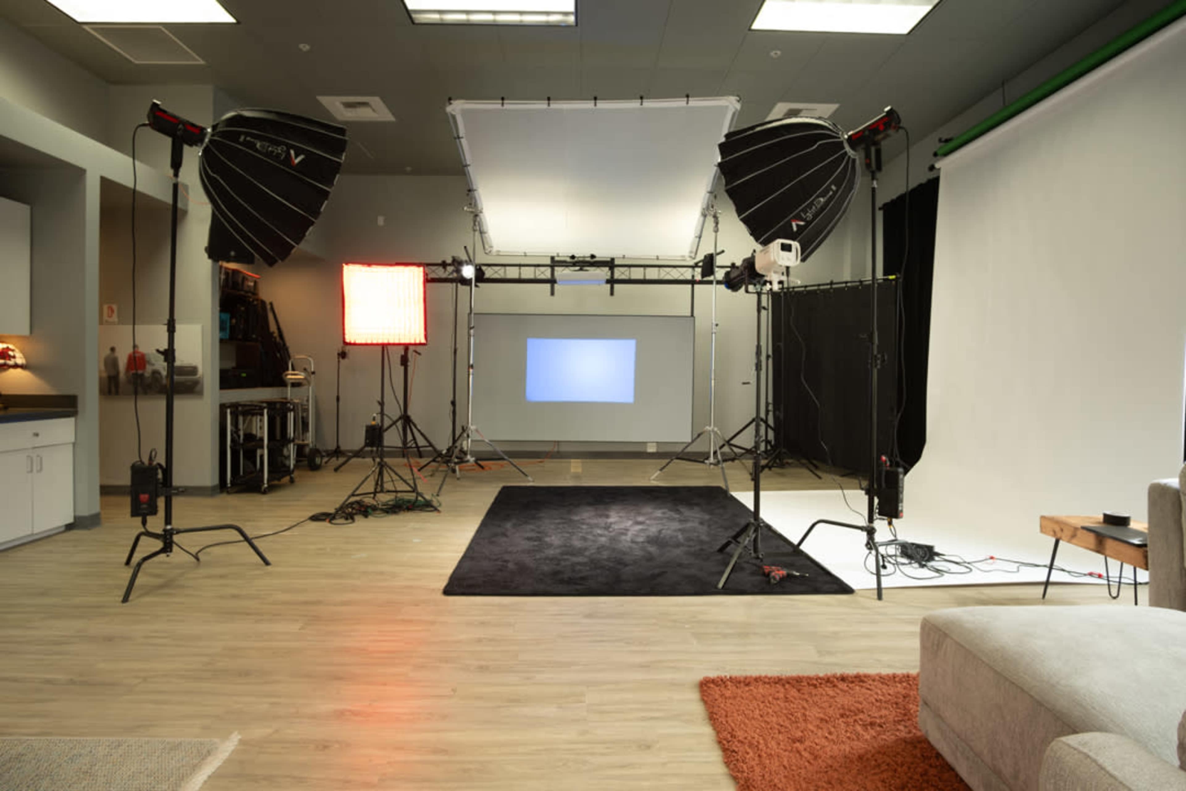 The image shows a photography studio setup with multiple light sources, backdrops, and a central softbox on a wooden floor.