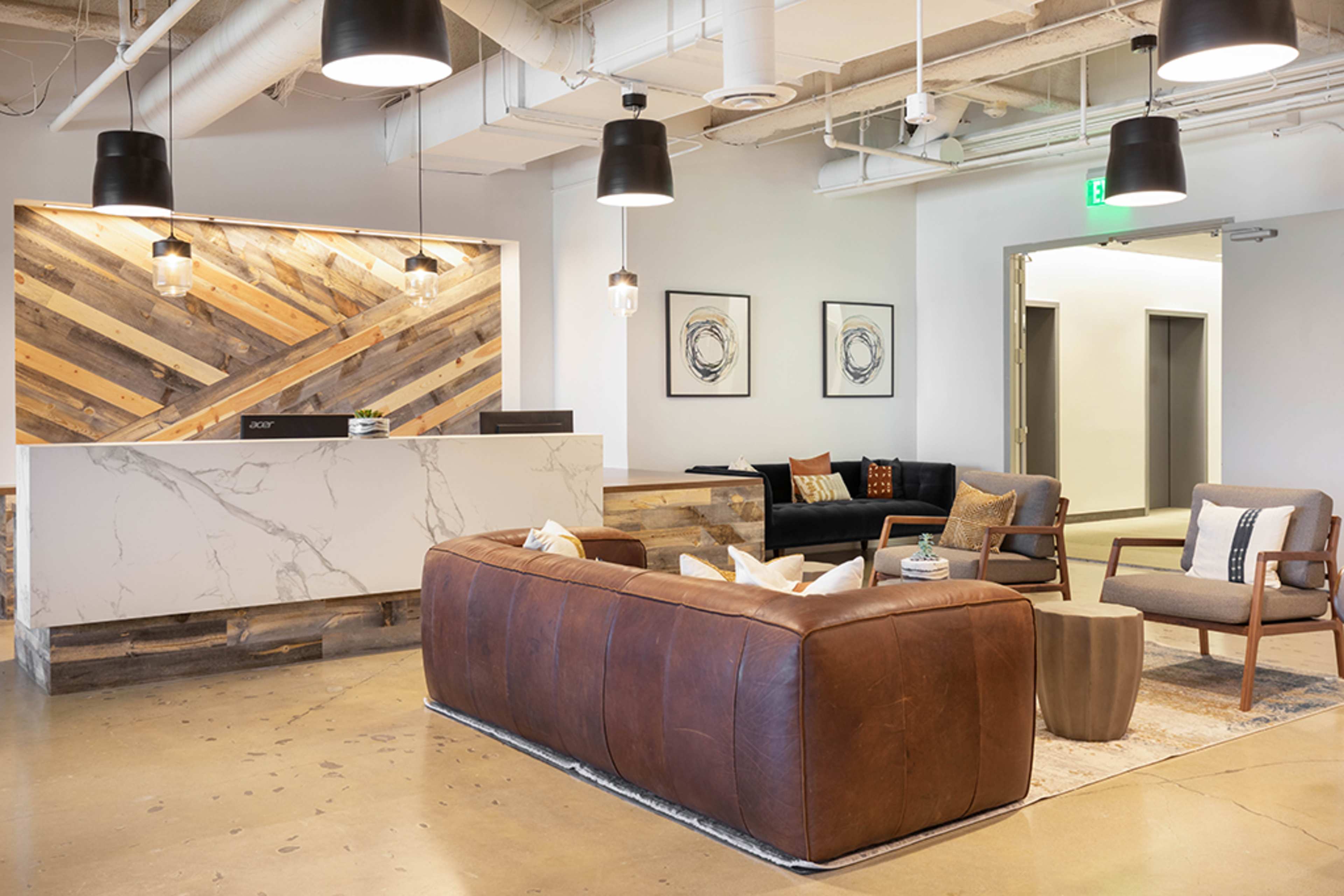 A modern reception area with a large leather sofa, two chairs, a coffee table, and a welcoming front desk against a patterned wooden wall.