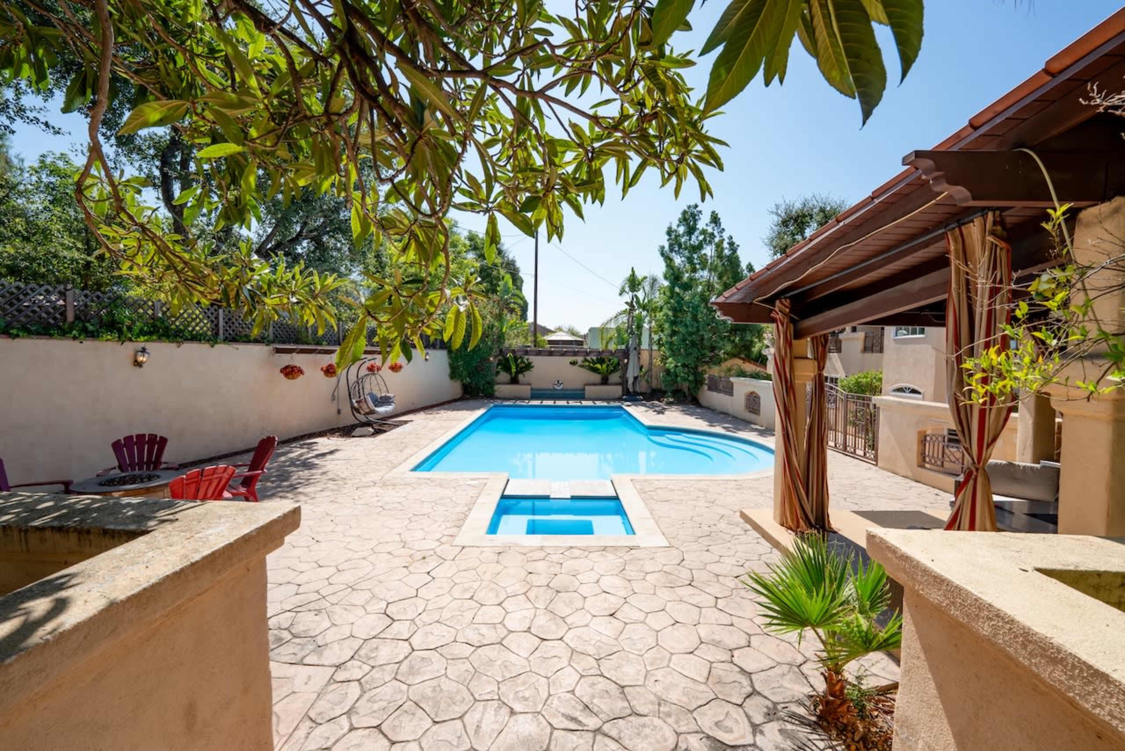 The image shows a backyard with a swimming pool surrounded by a stone patio and lounge chairs.