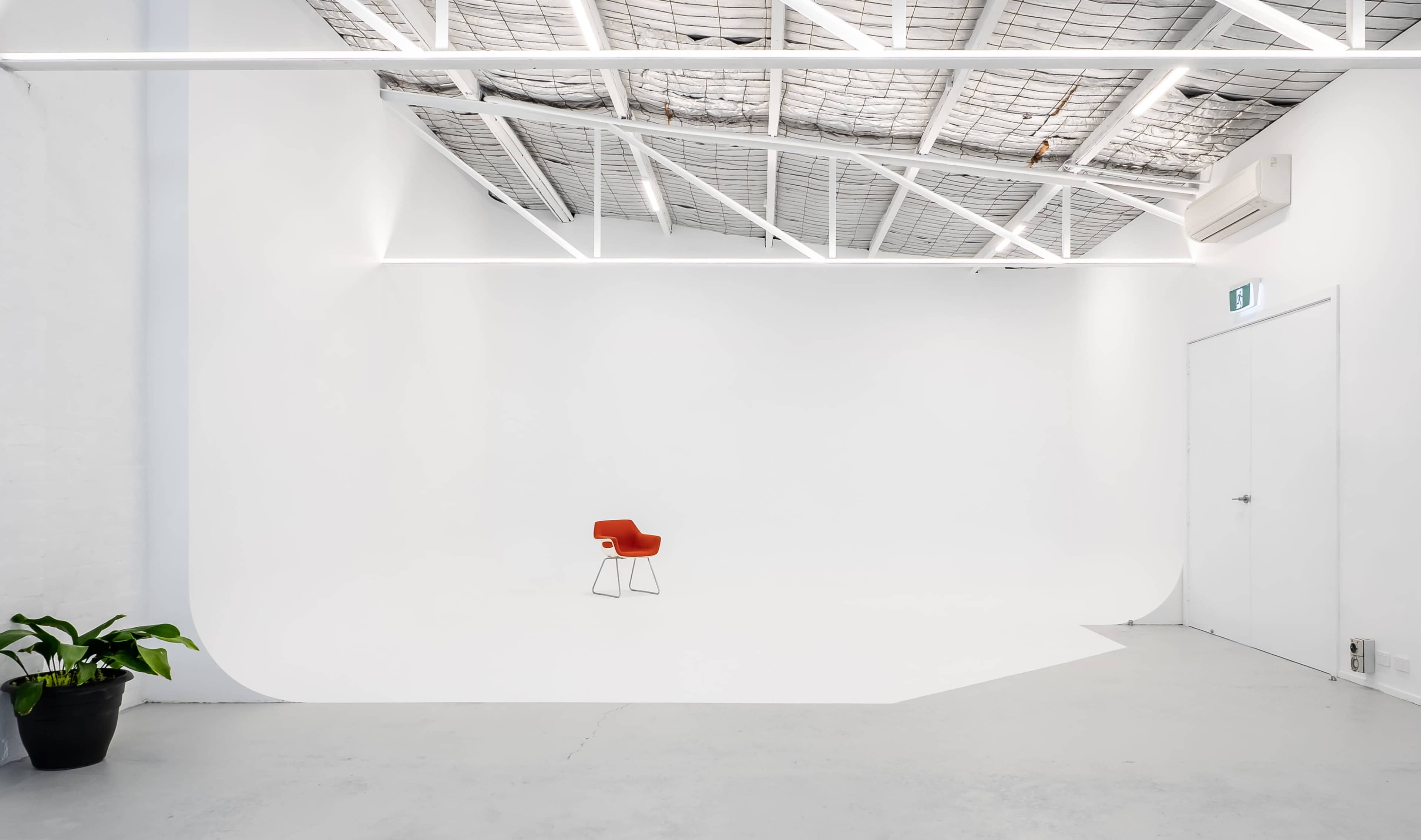 A minimalist studio with a single red chair positioned on a white backdrop, illuminated by overhead lights.