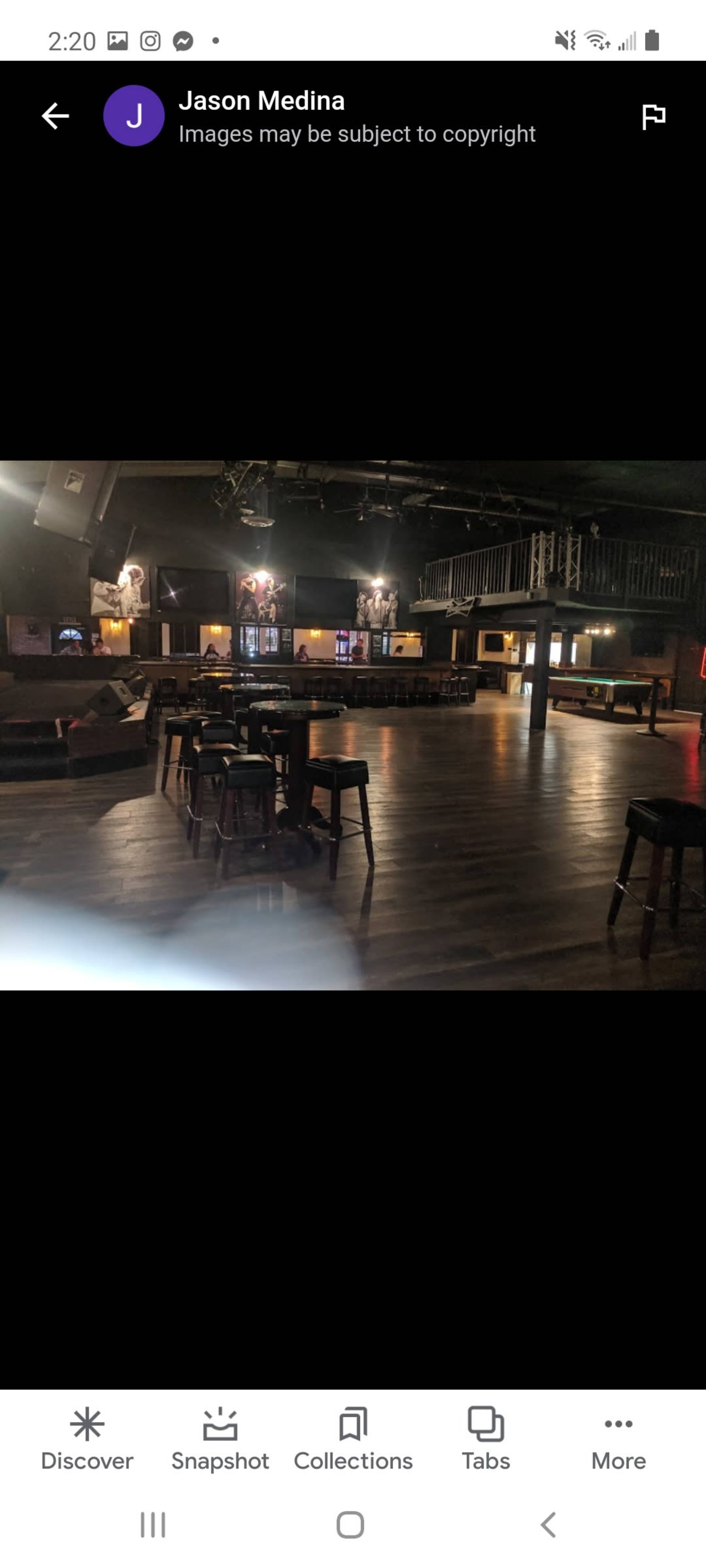 An empty music venue with wooden floors, tables, and a stage area in low lighting.