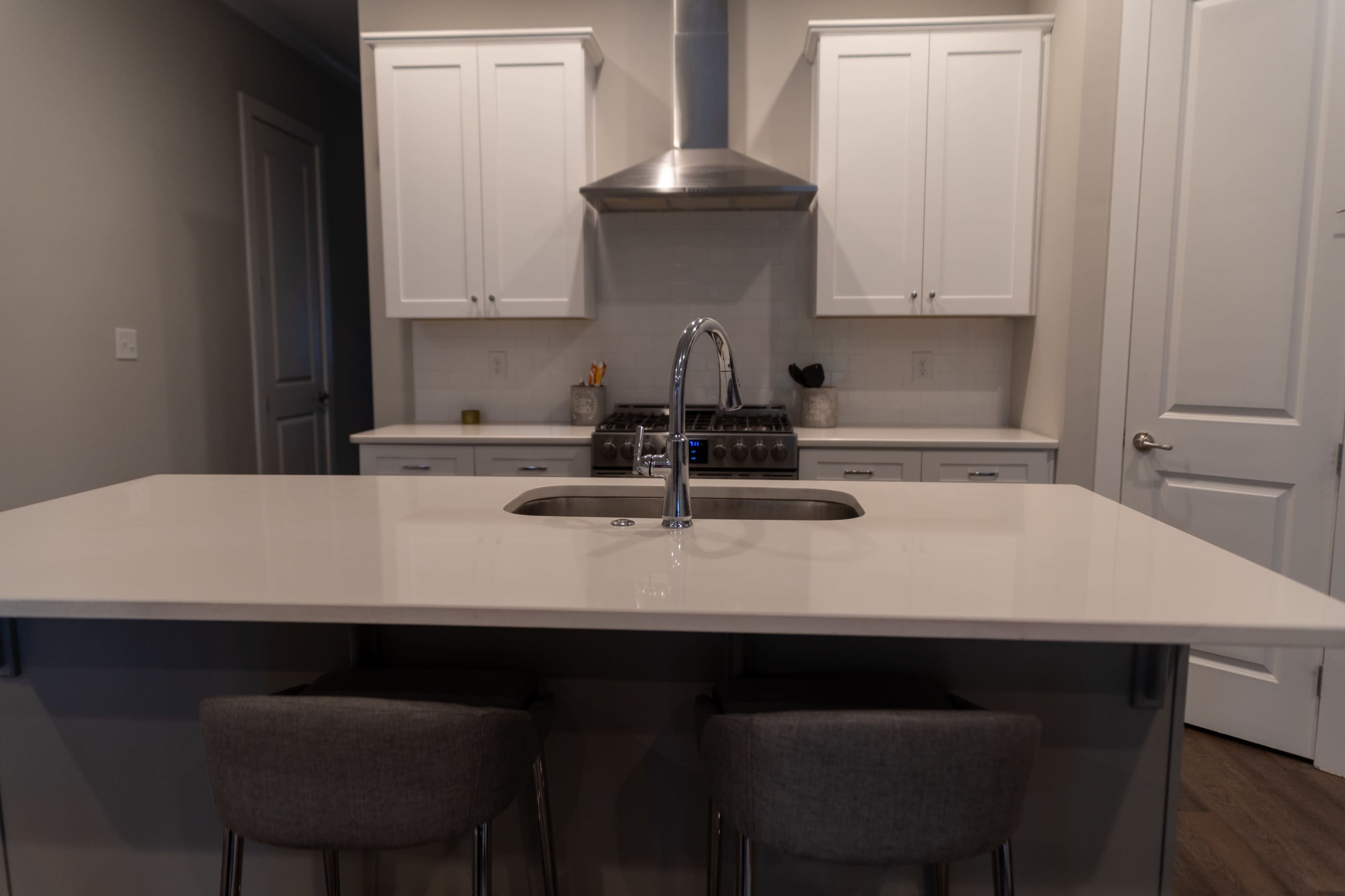 A modern kitchen features a large island with a double sink, surrounded by two bar stools, and cabinets above a stainless steel stove and hood.