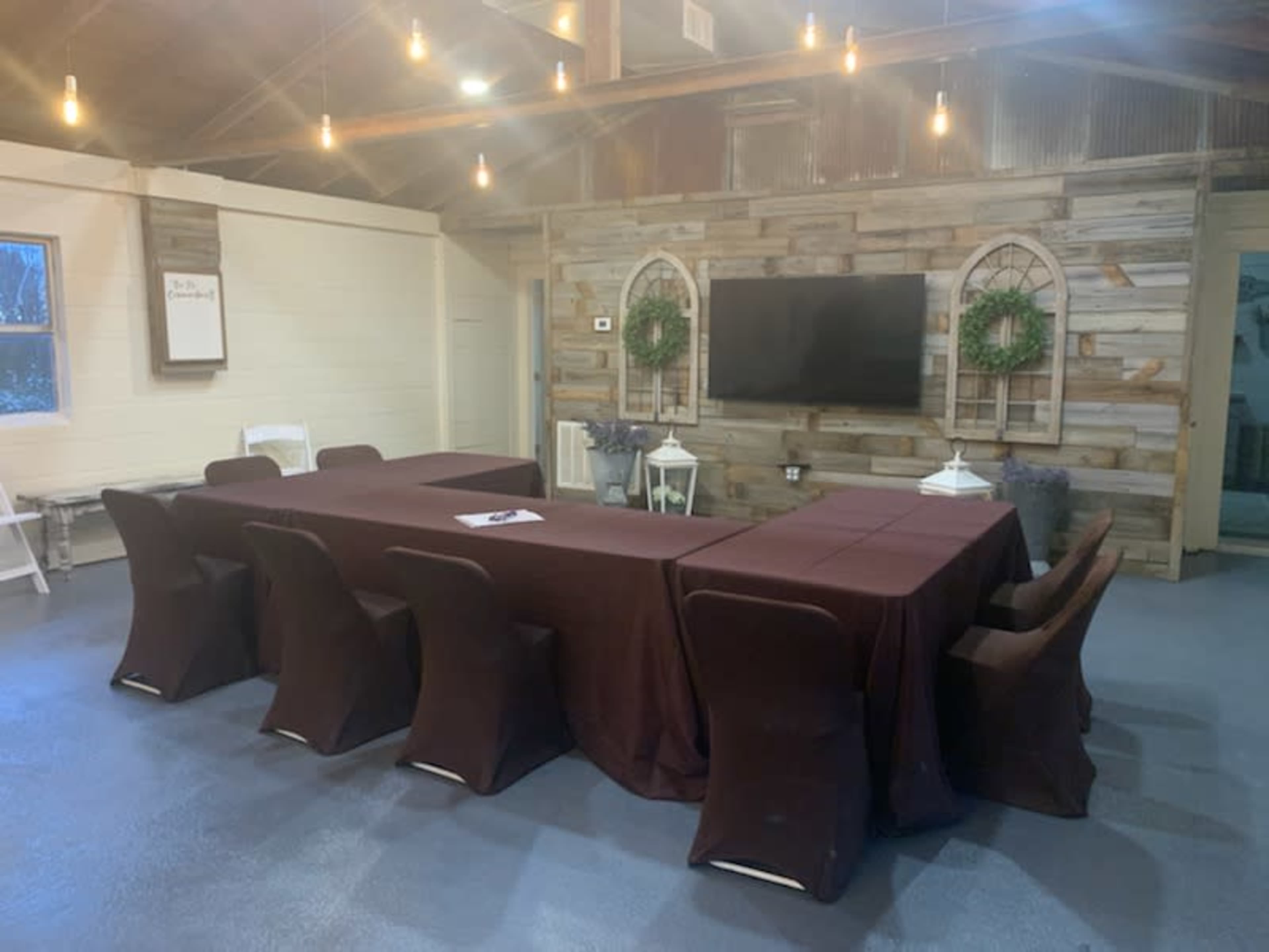 A long meeting table with dark table covers is set up in a room featuring a wooden accent wall and a large television on display.