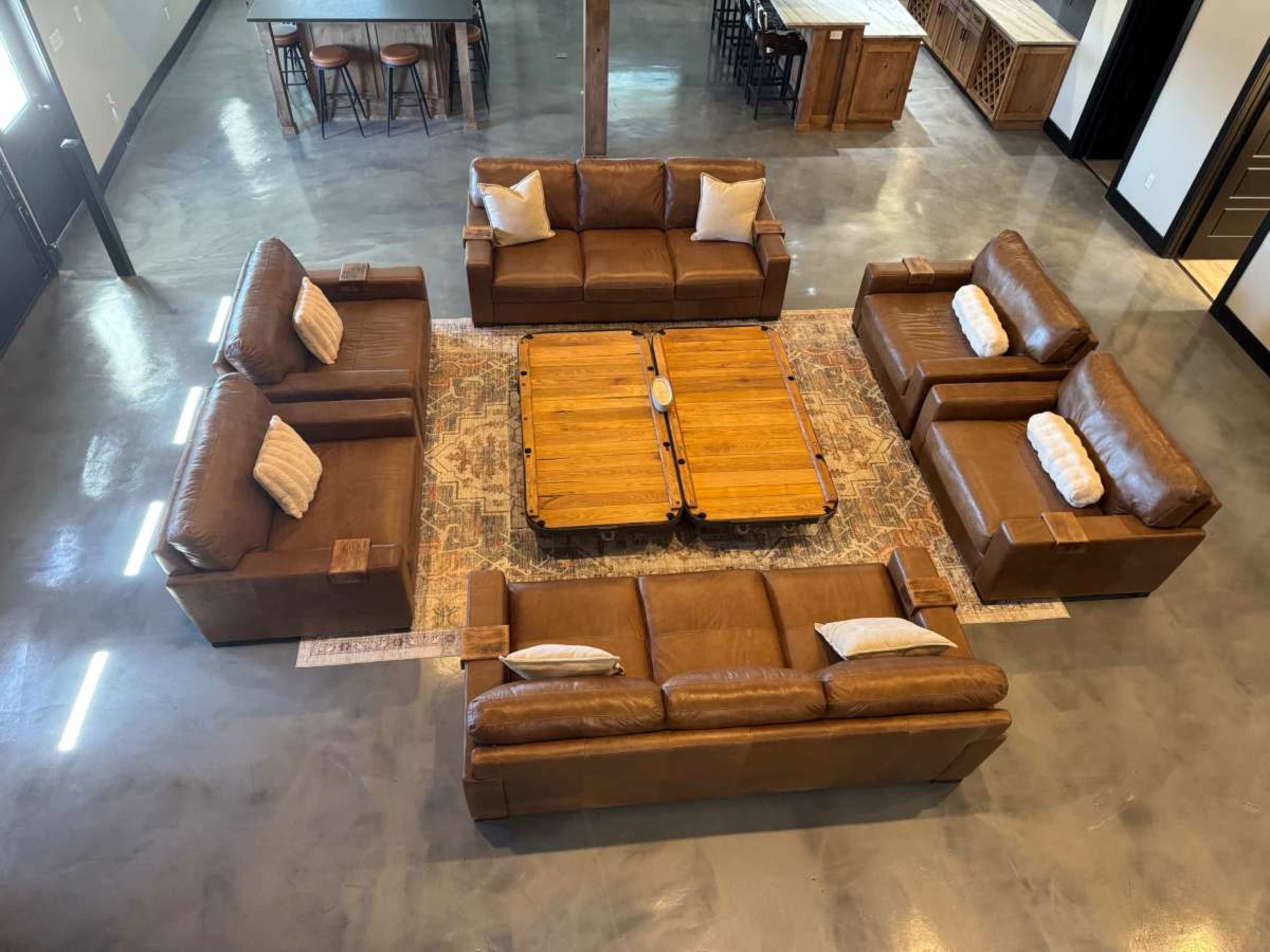 The image shows a spacious living area featuring two sets of brown leather sofas arranged in a circular formation around a wooden coffee table on a patterned rug.