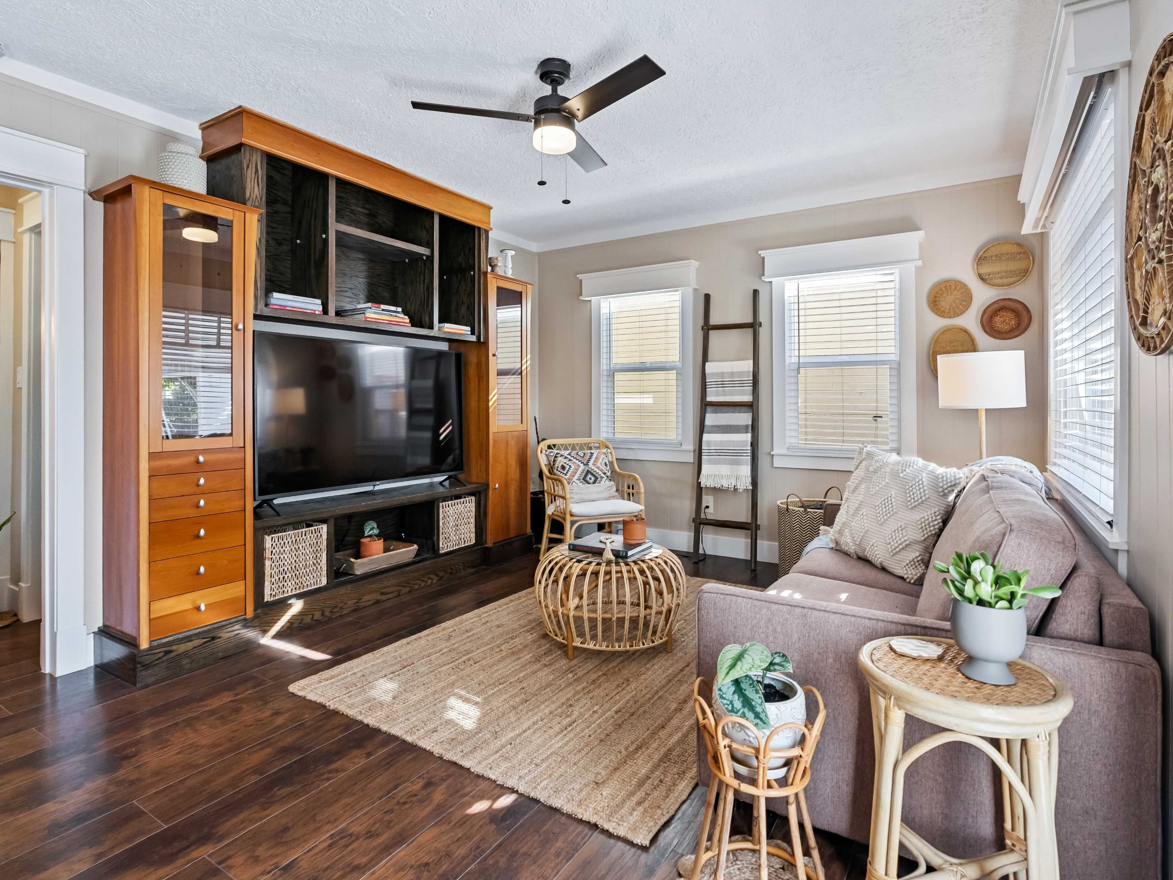 The living room features a television stand with storage, a sofa, a rattan coffee table, and decorative wall elements.