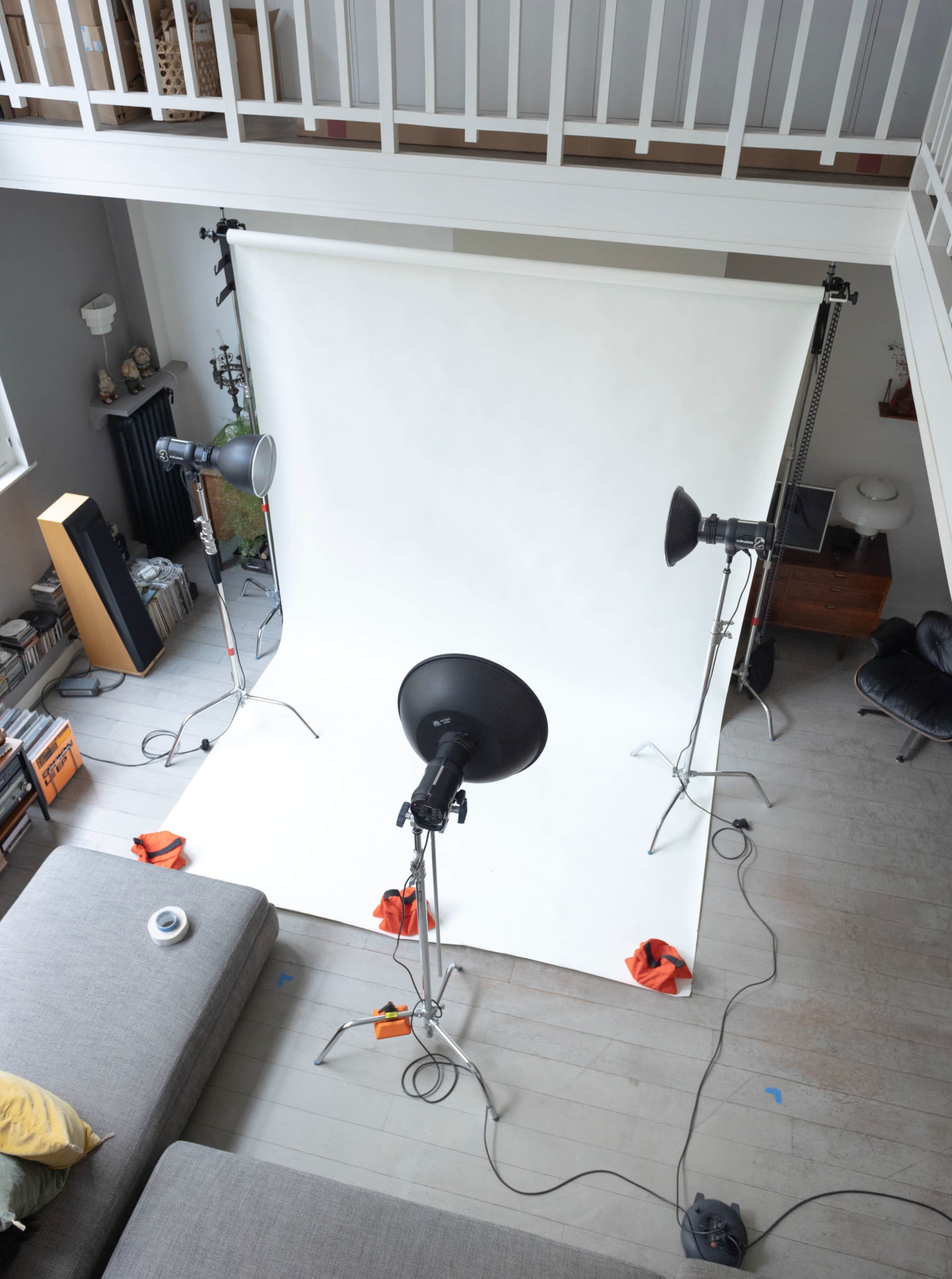 A photography studio setup features a backdrop with multiple studio lights positioned around a white backdrop on a wooden floor.