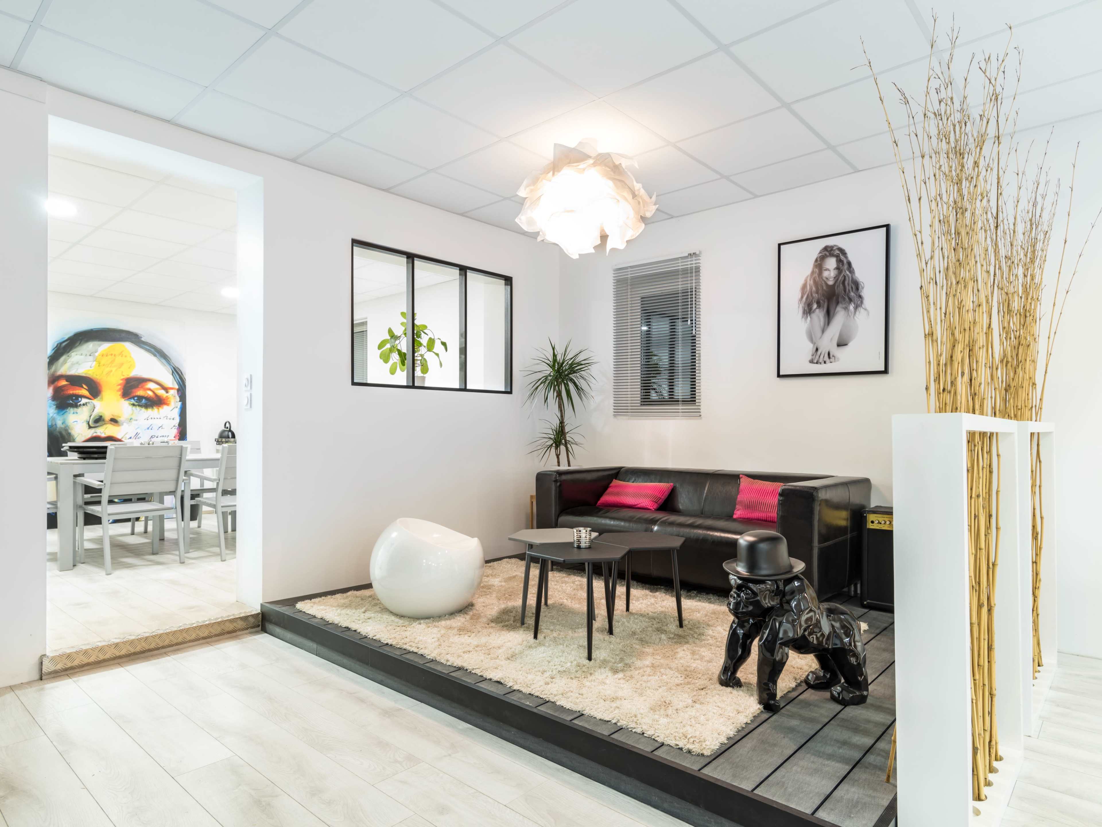 The image shows a modern living room with a black leather sofa, a round white coffee table, and a decorative black dog statue beside a light-colored rug.