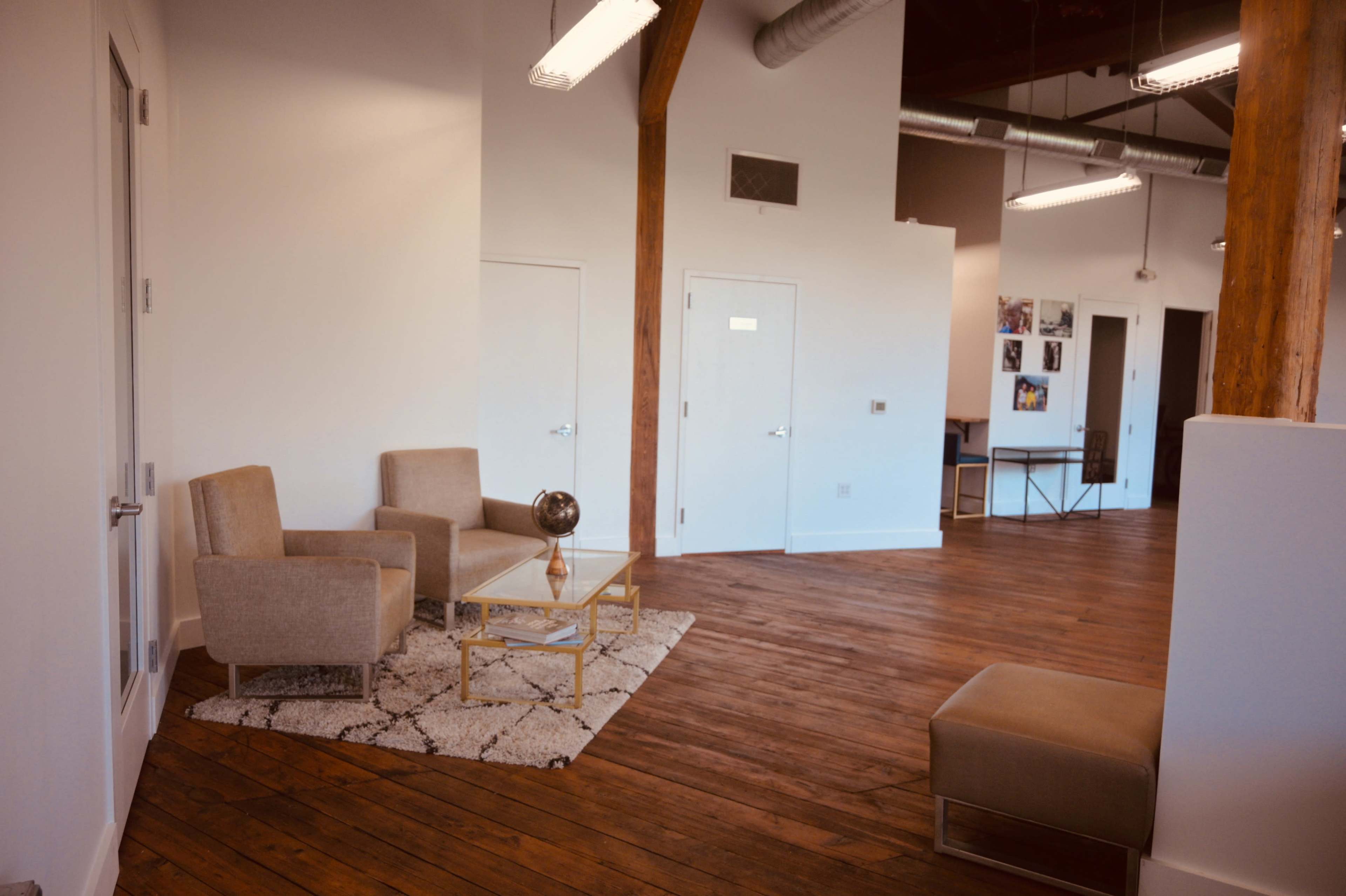 A spacious interior features two light-colored chairs, a small coffee table, and wooden flooring, with white walls and doorways in the background.
