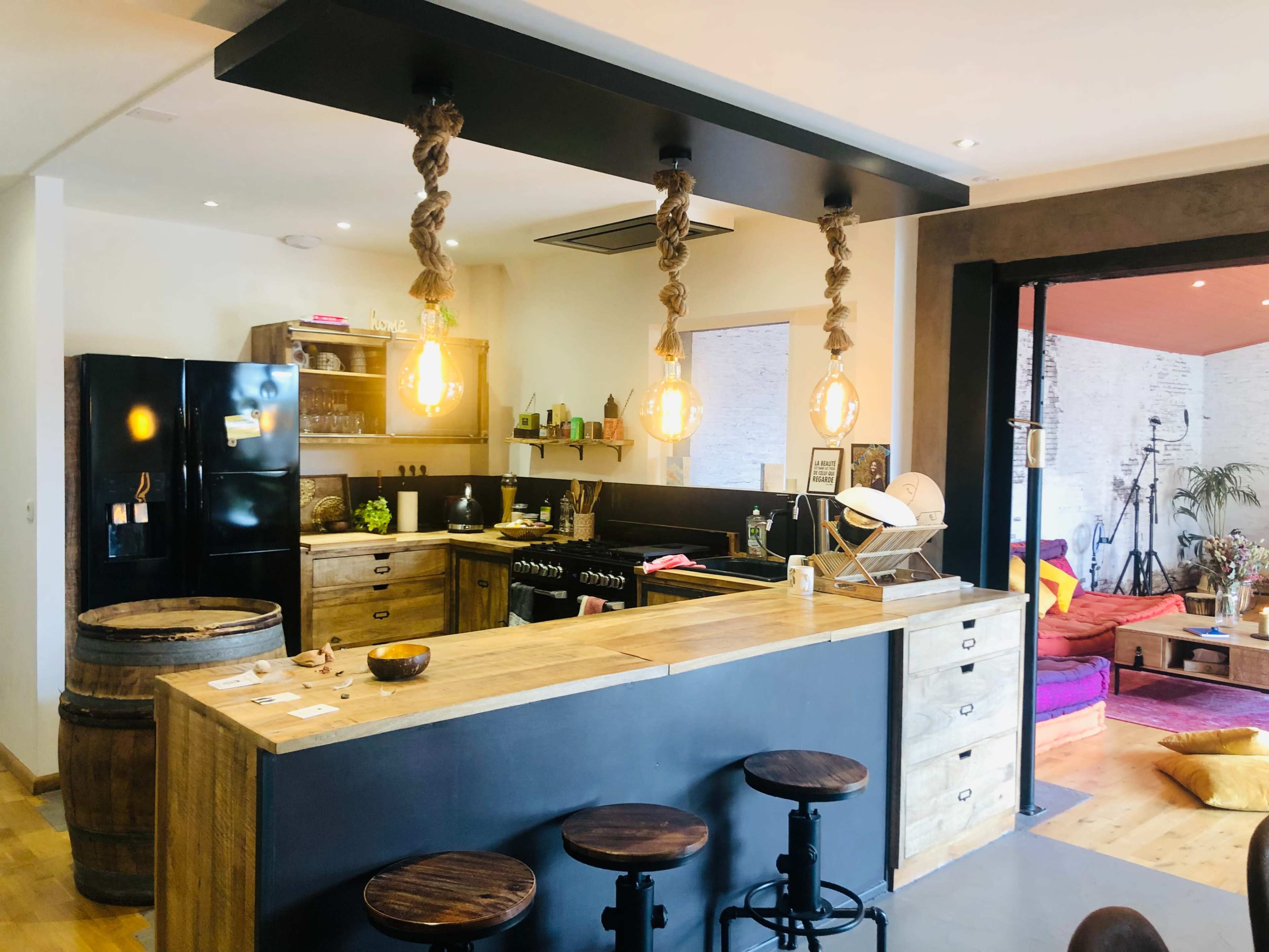 The image shows a modern kitchen with a wooden island, black cabinetry, hanging light fixtures, and a bar area with stools.