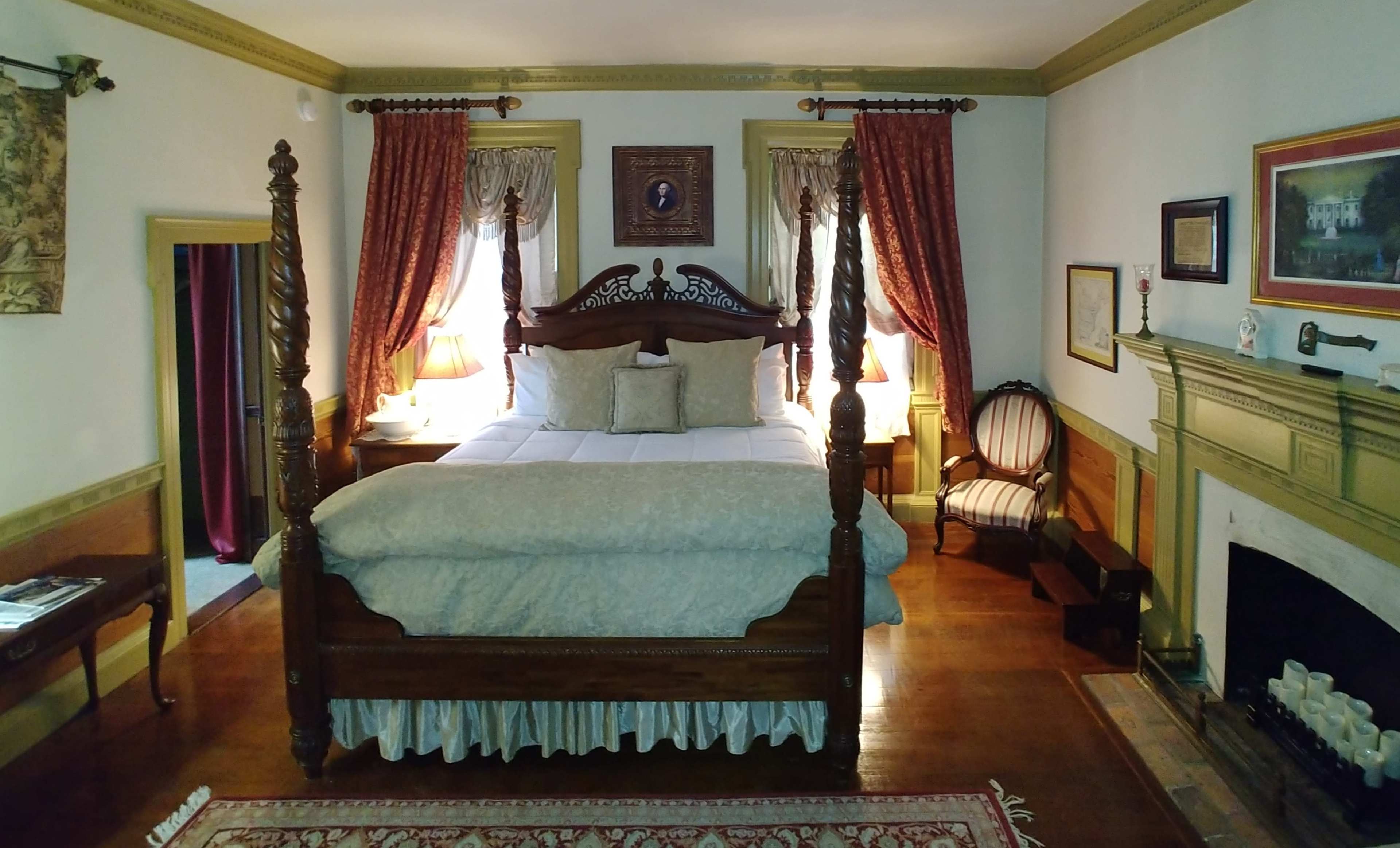 A bedroom with a four-poster bed, decorative curtains, a fireplace, and a seating area.