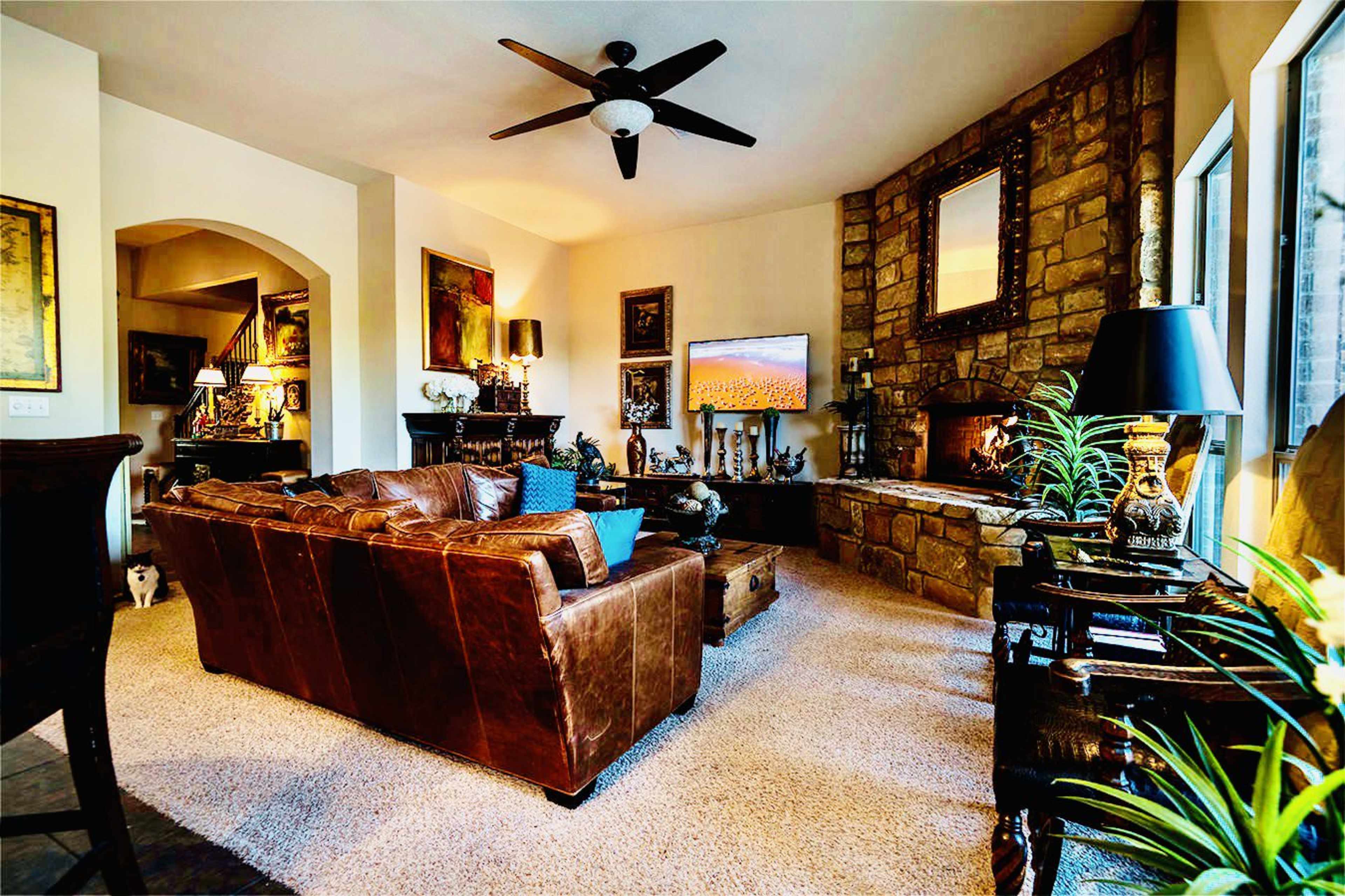 A cozy living room features a leather sofa, a stone fireplace, and various decorative items arranged around a television mounted on the wall.