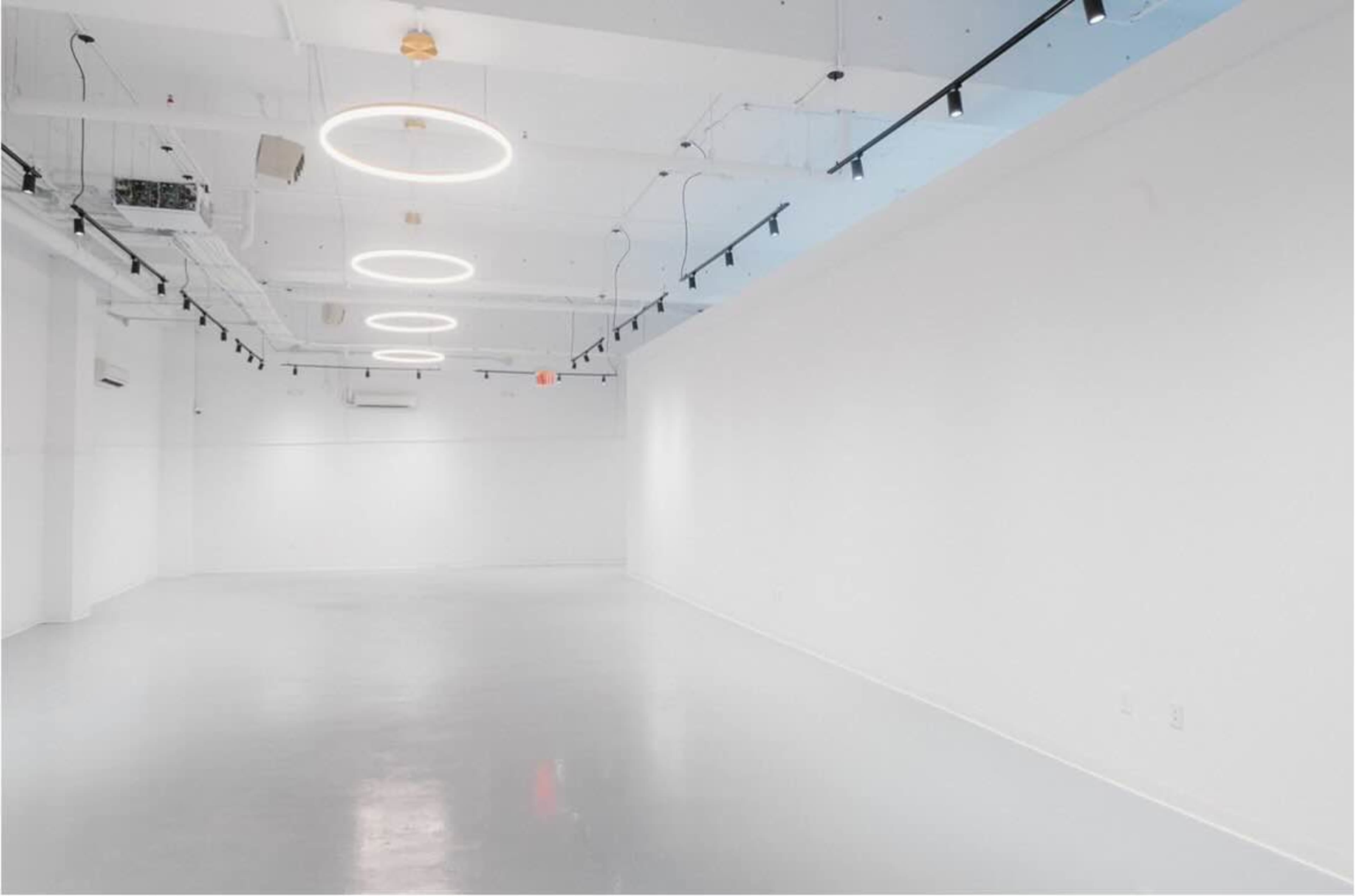 The image shows a spacious, brightly lit room with white walls and a polished floor, featuring circular overhead lights.