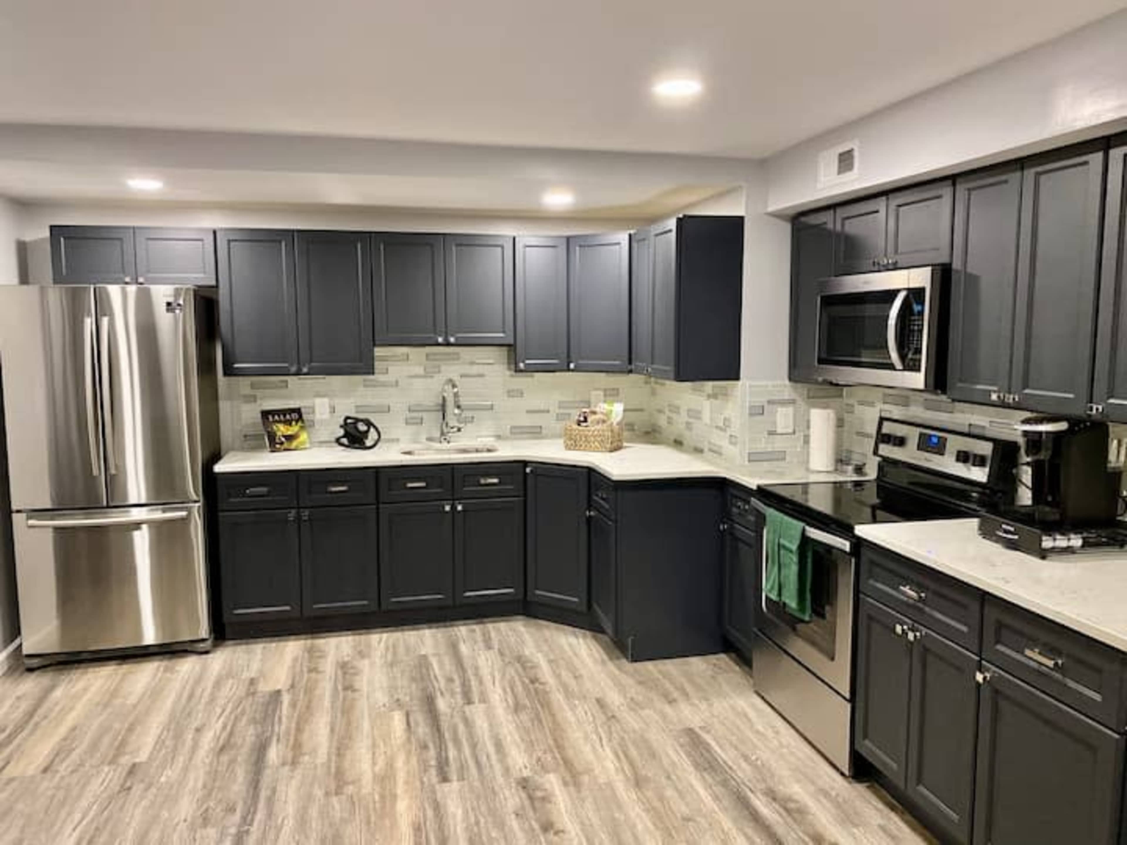 A modern kitchen with dark cabinets, stainless steel appliances, and a light-colored countertop.