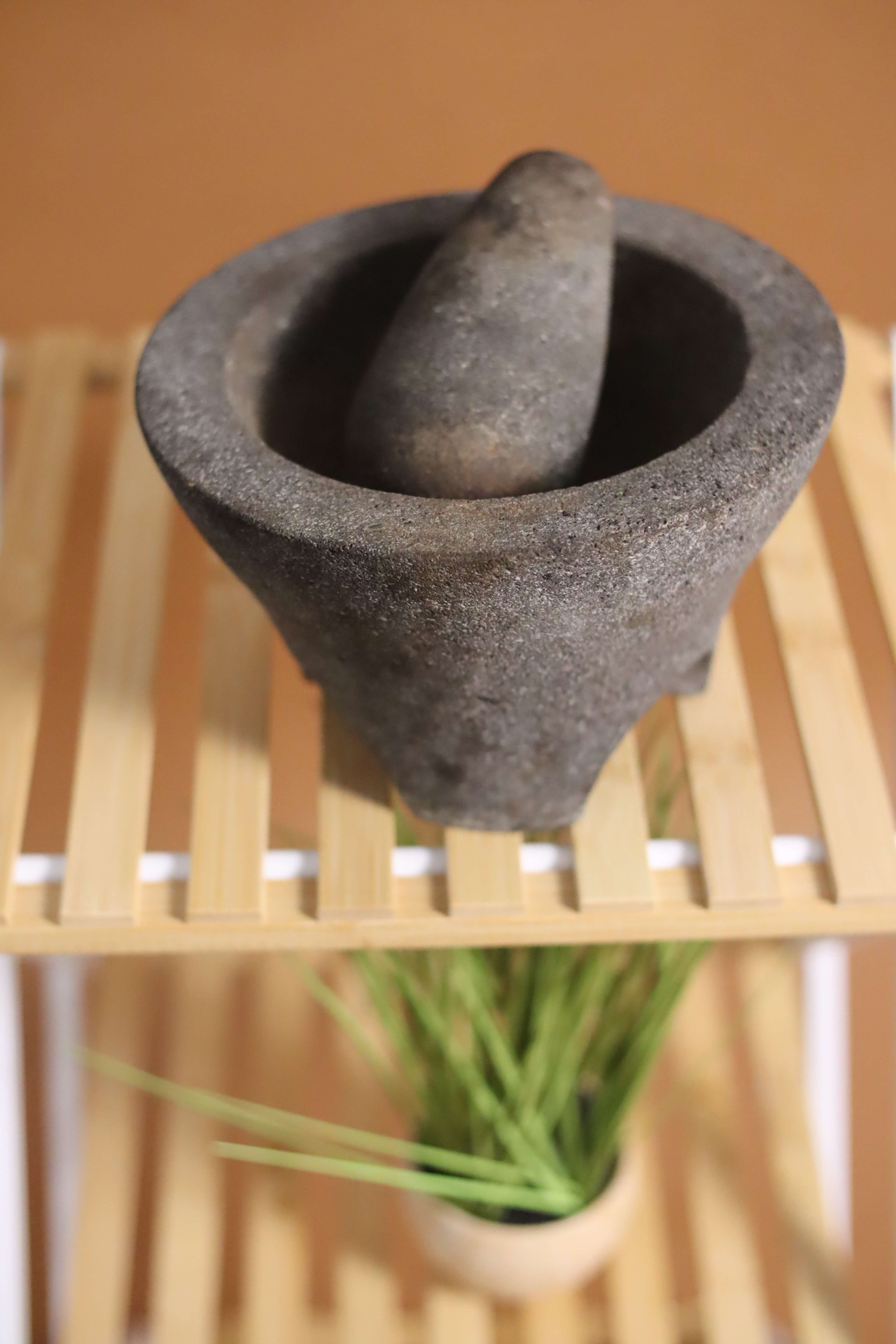 A stone mortar and pestle sit on a wooden shelf above a small potted plant.