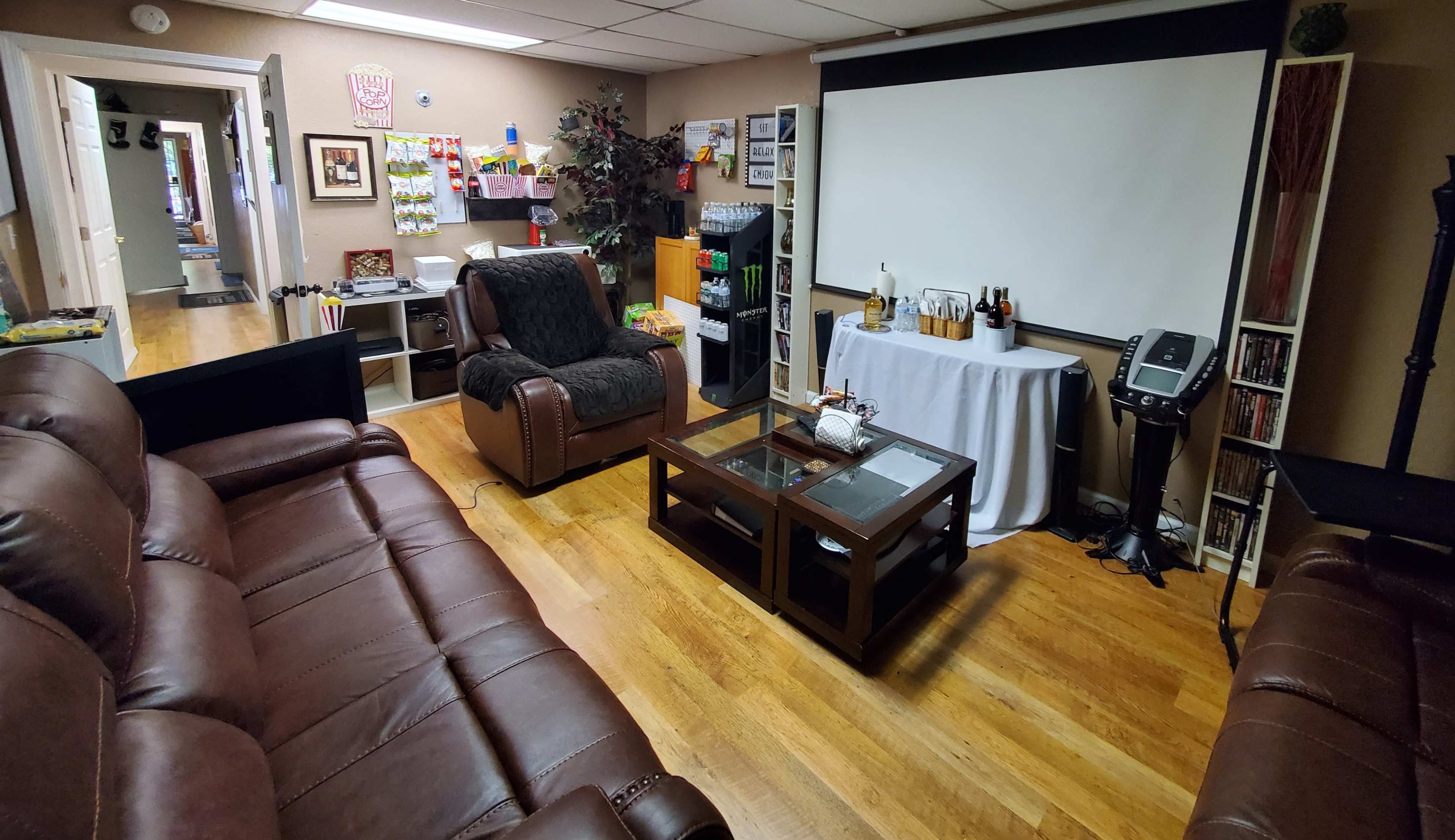 A cozy living room featuring brown leather sofas, a recliner, a projector screen, and a coffee table with various items on it.