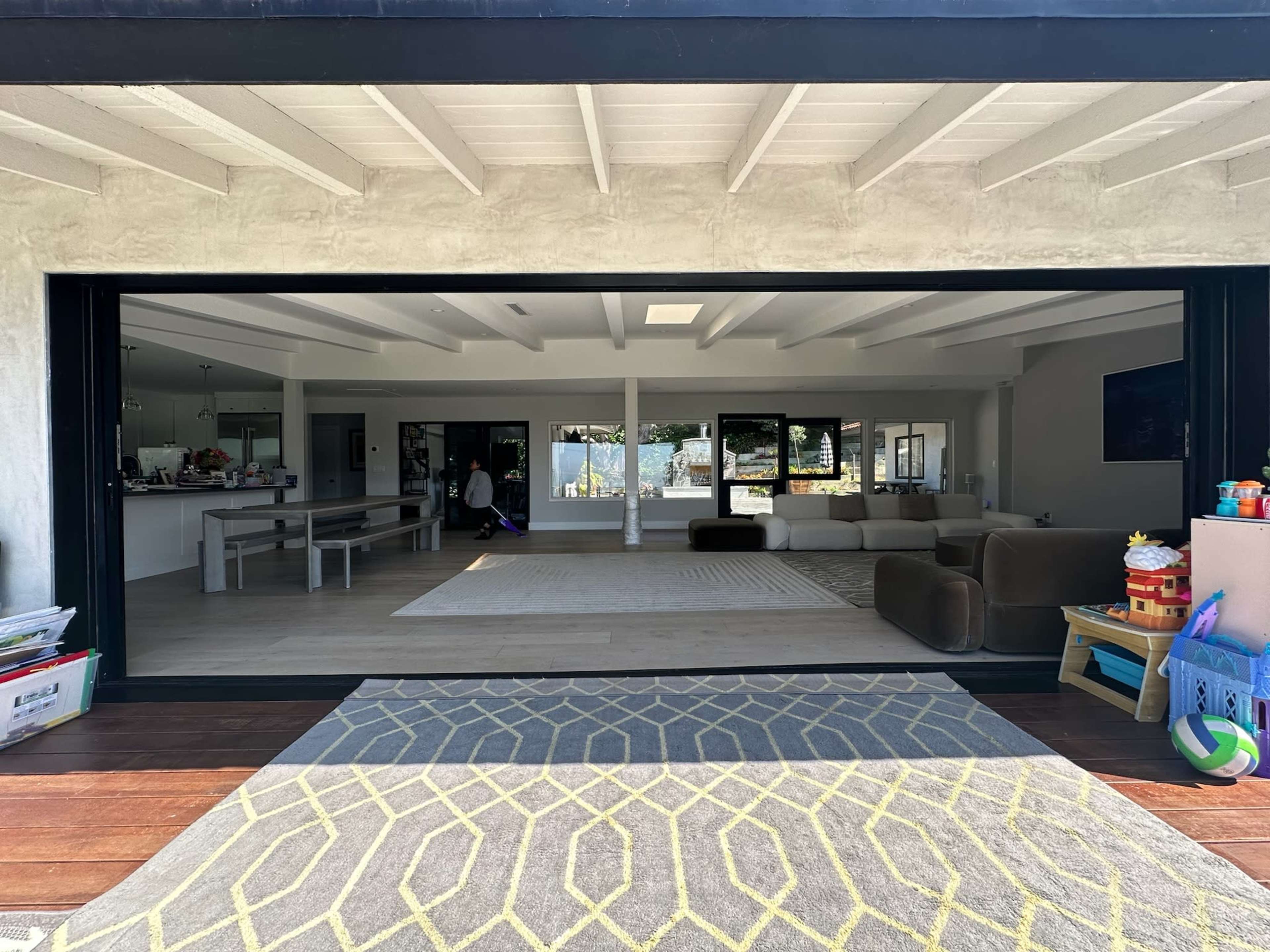An open living space with a view extending from a patterned outdoor rug through large sliding glass doors into a modern interior featuring a seating area and dining table.