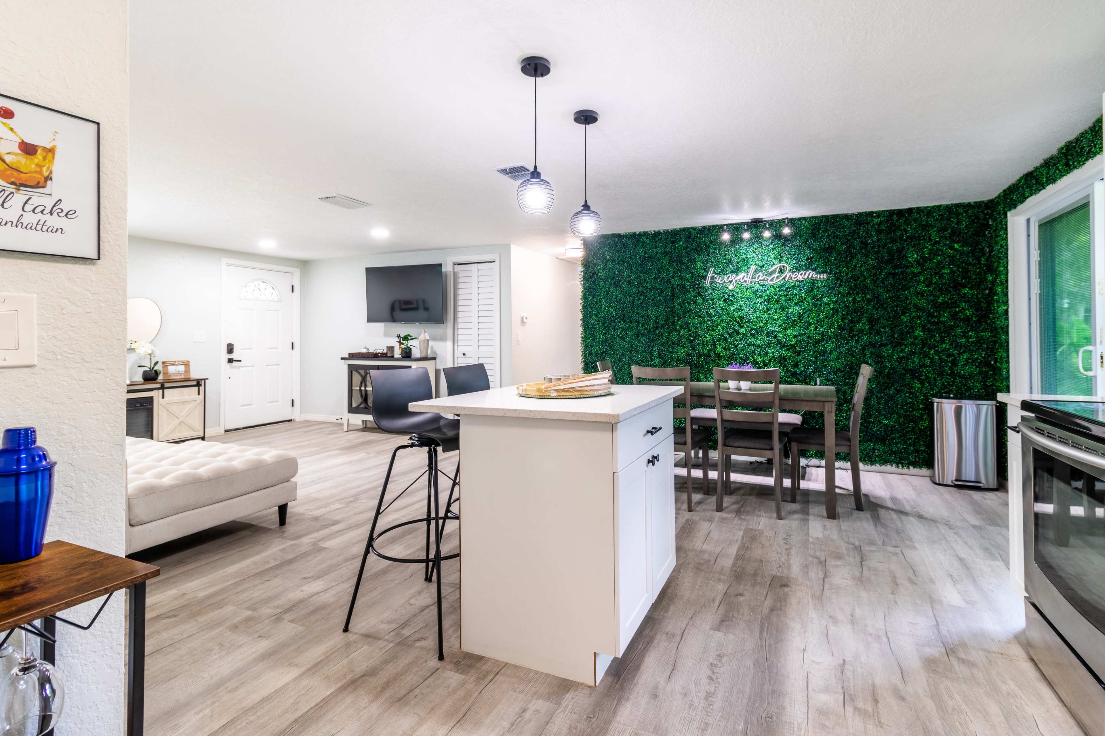 A modern kitchen and dining area featuring a white island, wooden dining table, and a green wall with decorative plants.