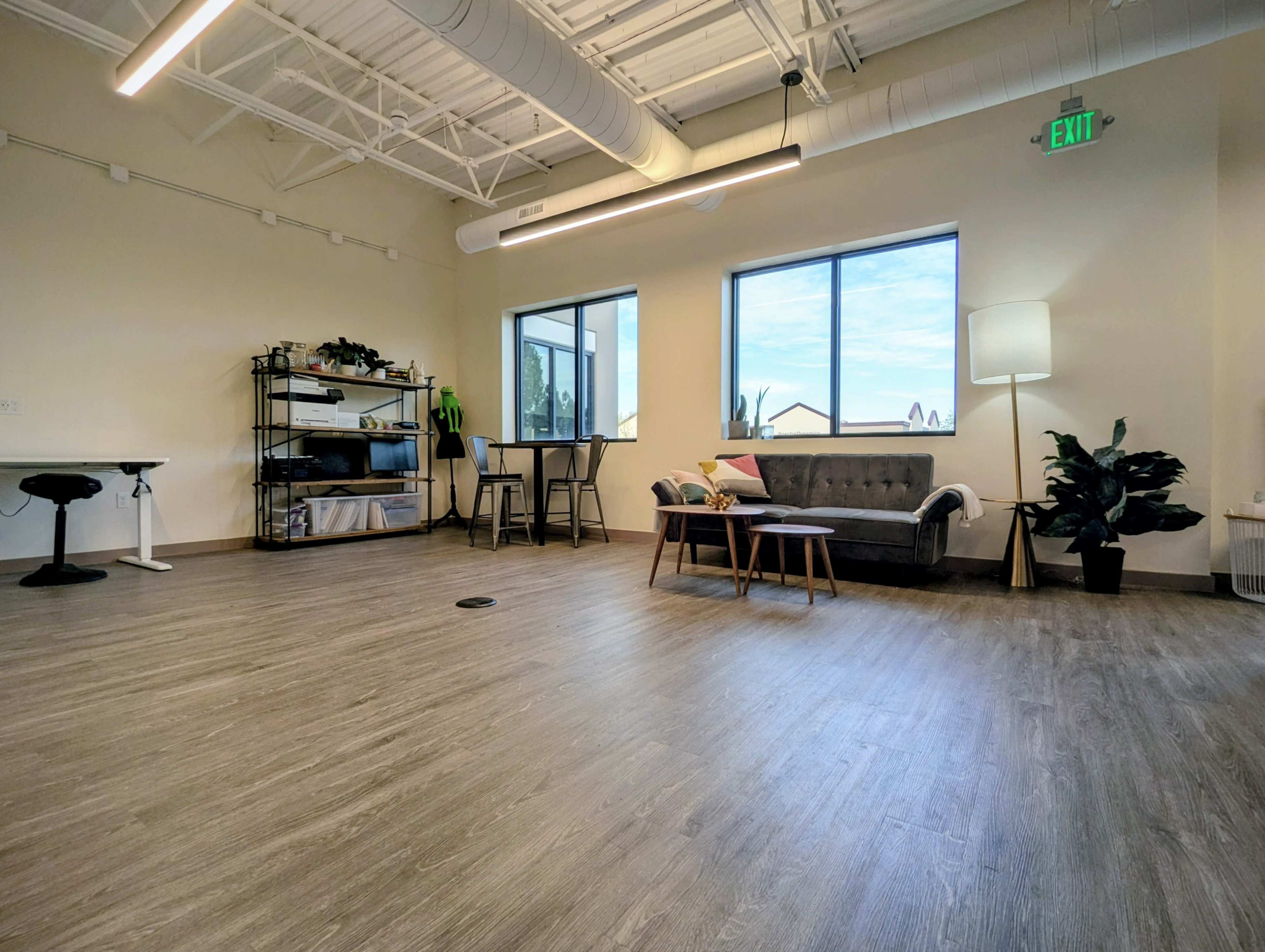 The image depicts a modern, spacious interior with wooden flooring, a couch, a coffee table, and large windows allowing natural light.