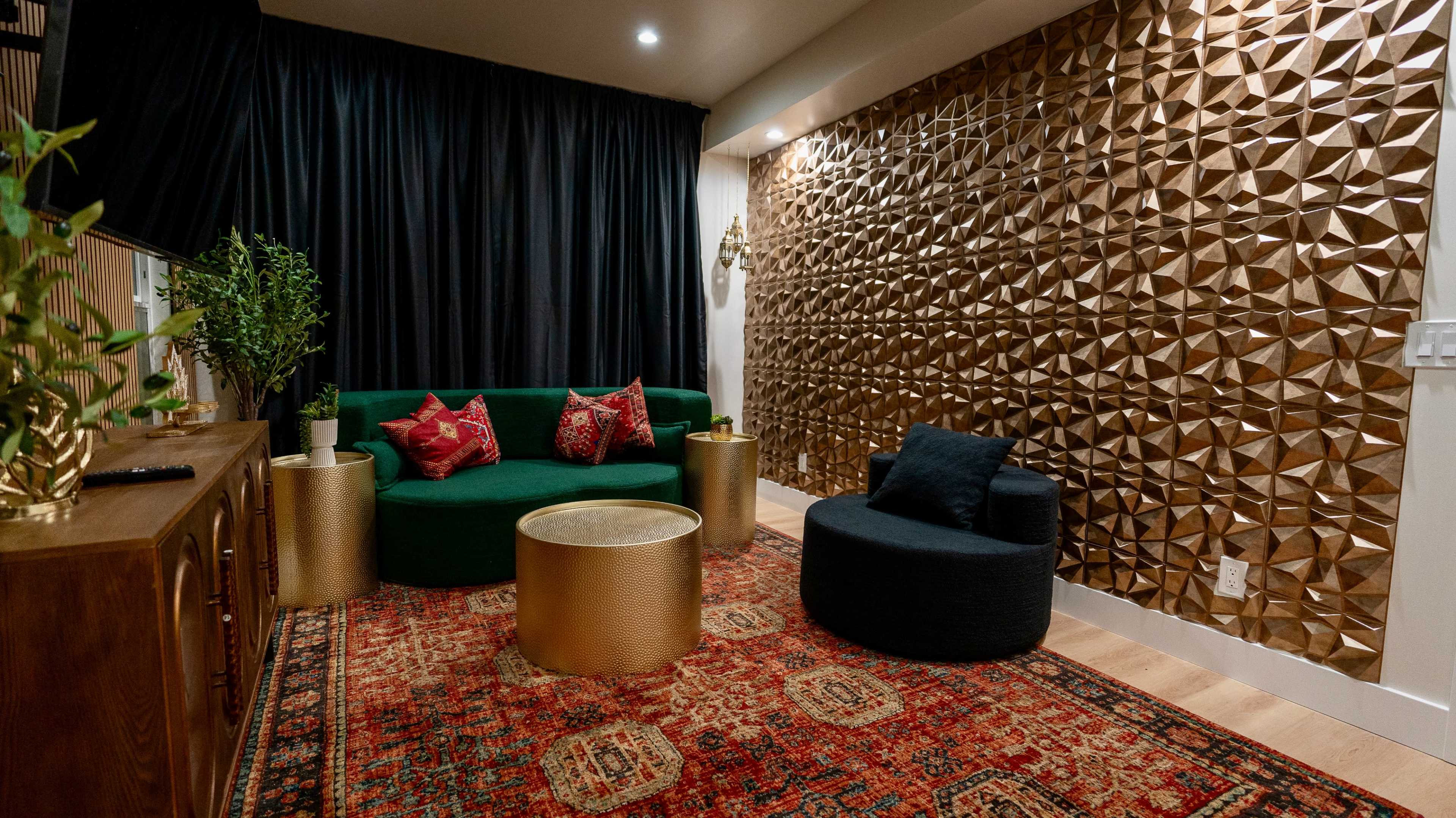 The image shows a contemporary living room featuring a green sofa and a round black chair, both placed on a decorative rug in front of a textured gold wall.