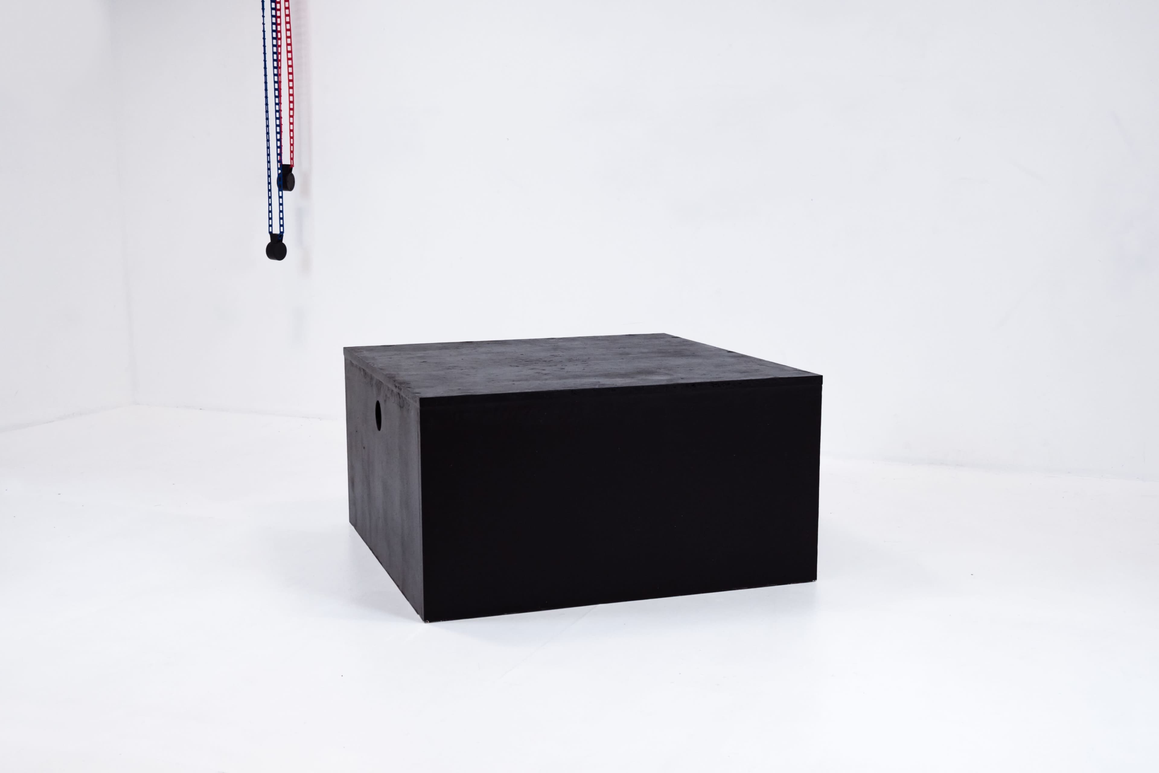 A black square box is positioned in the center of a minimalistic white room.