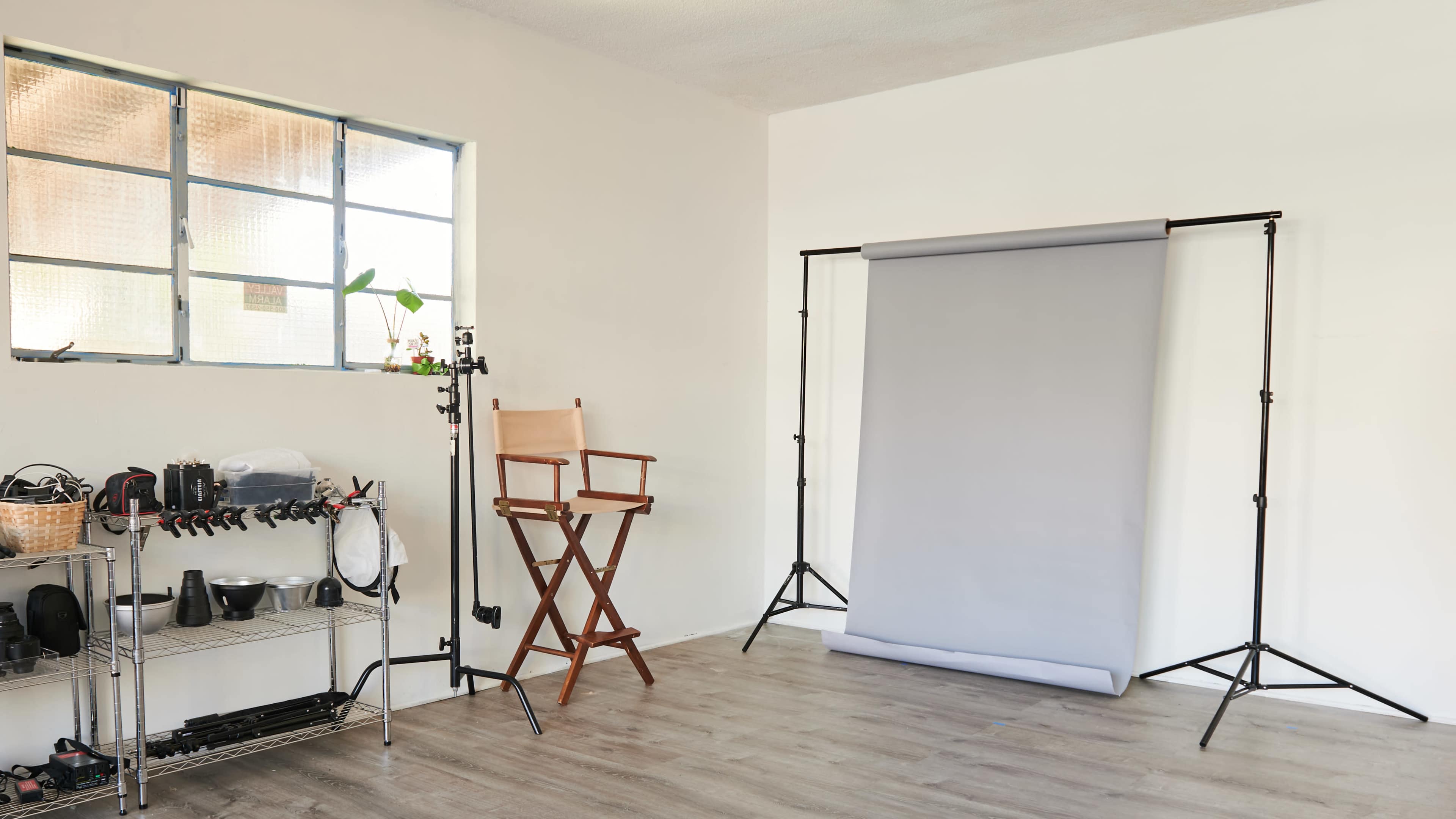 A photography studio with a gray backdrop setup, a director's chair, and various equipment neatly arranged on a shelf.