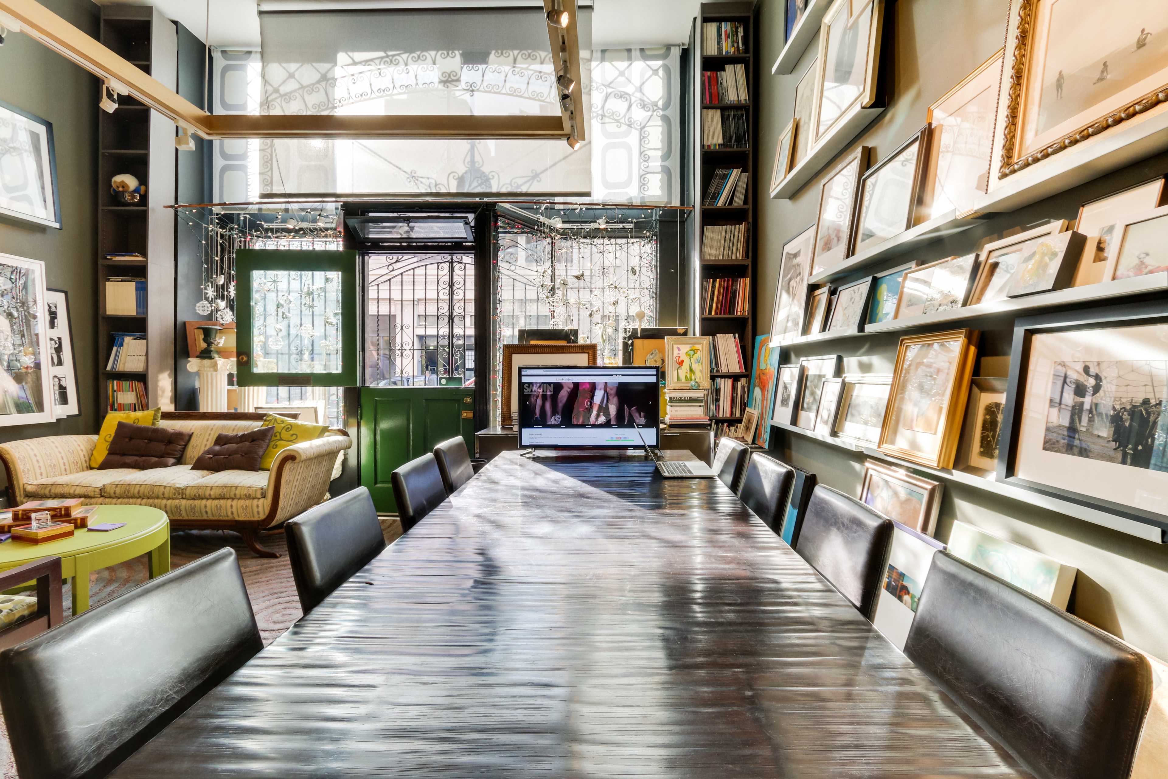 A spacious room with a long table surrounded by black chairs, a laptop on the table, and walls adorned with various framed pictures.