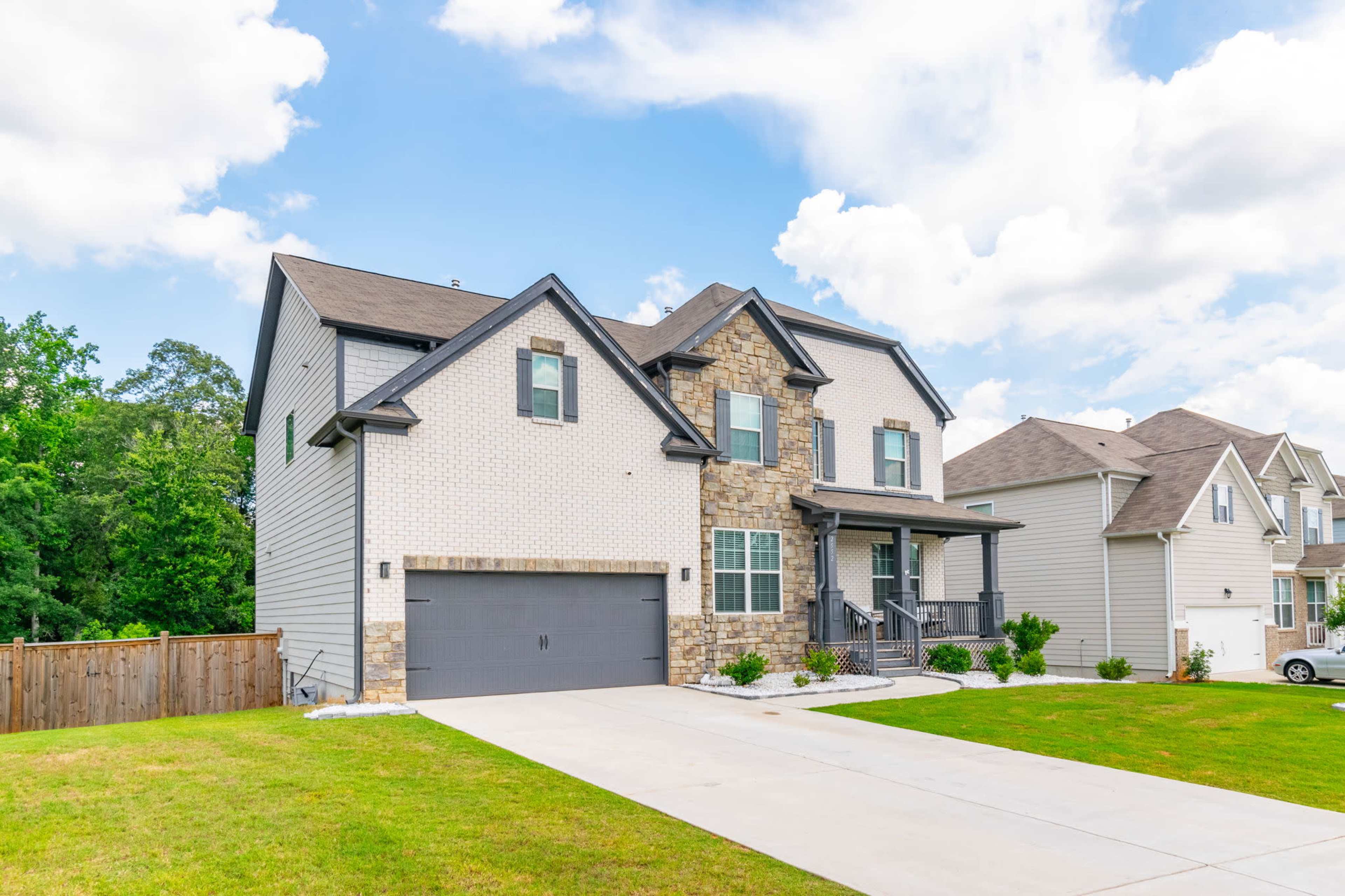 A two-story residential house with a stone and siding exterior, a landscaped front lawn, and a double garage sits on a paved driveway.