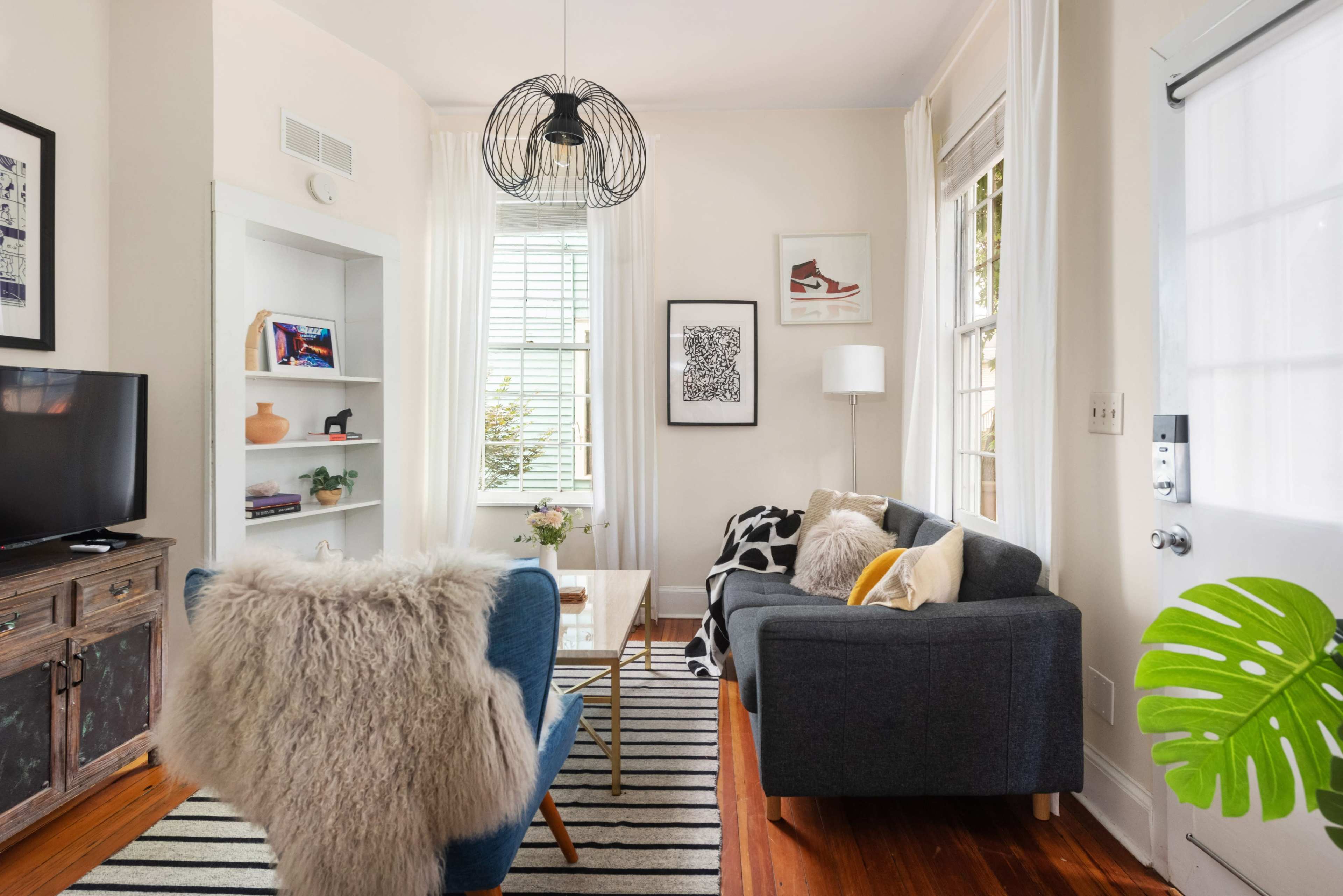 The living room features a mix of furniture, including a blue chair, a gray sofa, and a coffee table, with decorative items on display against a backdrop of light walls and a striped rug.