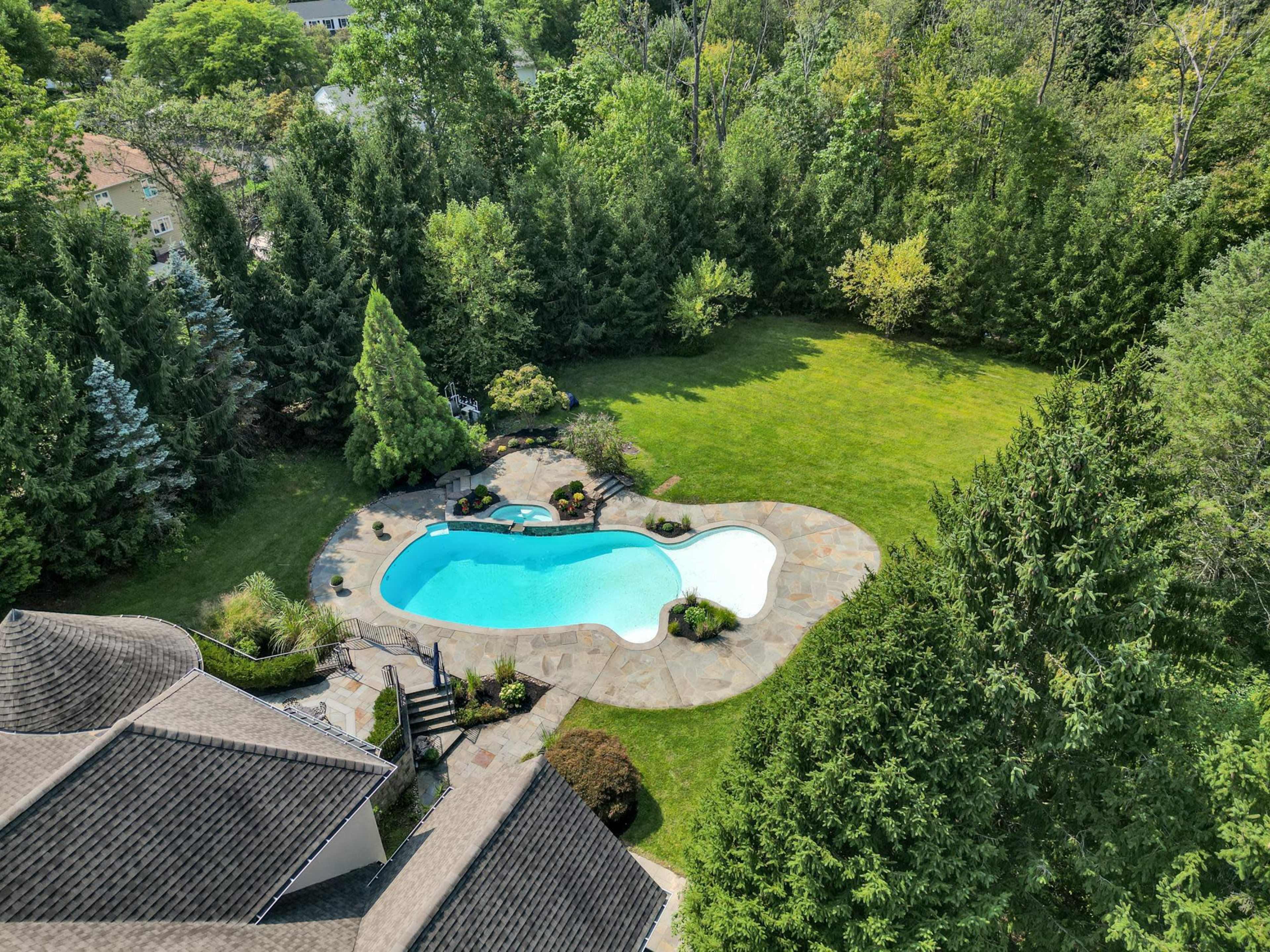 The image shows an aerial view of a backyard featuring a swimming pool surrounded by a stone patio and landscaped greenery.