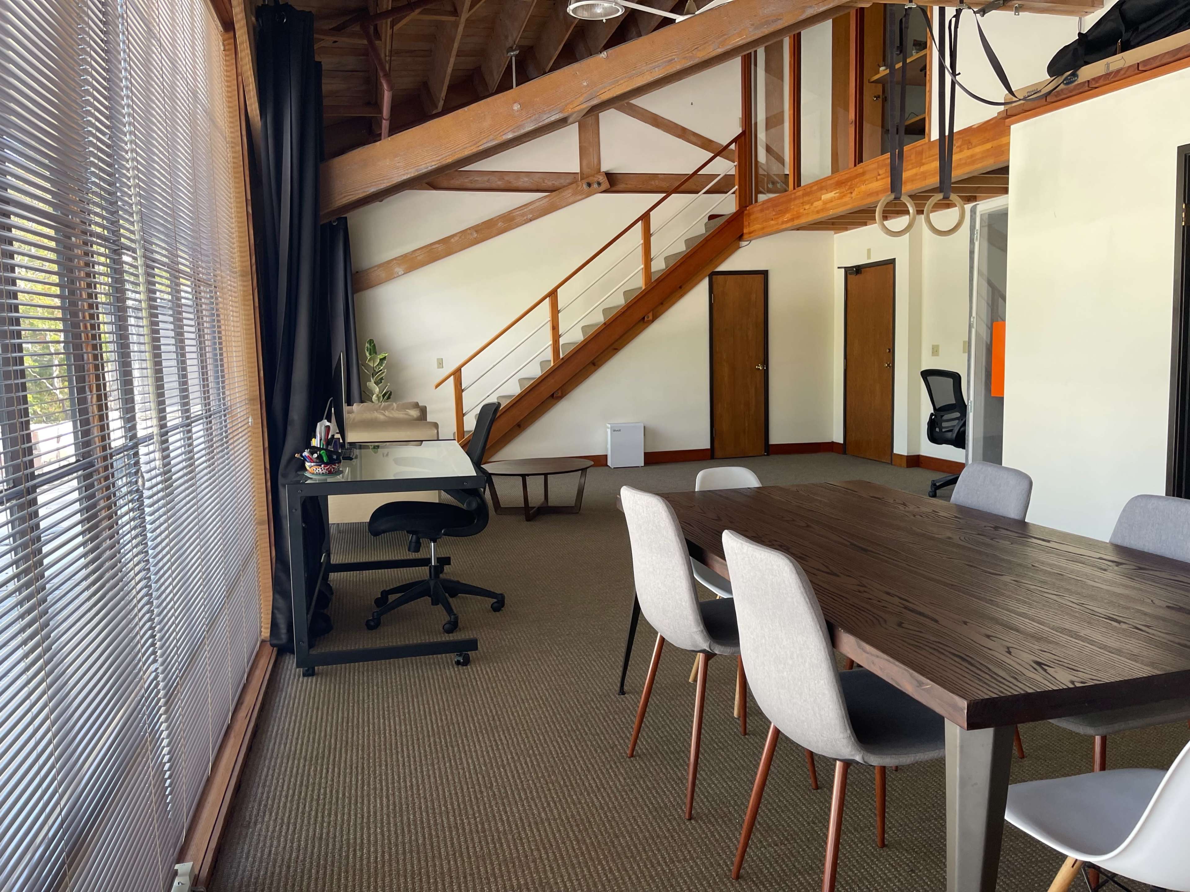 An office space featuring a dining table, chairs, a desk, and a staircase leading to an upper level.