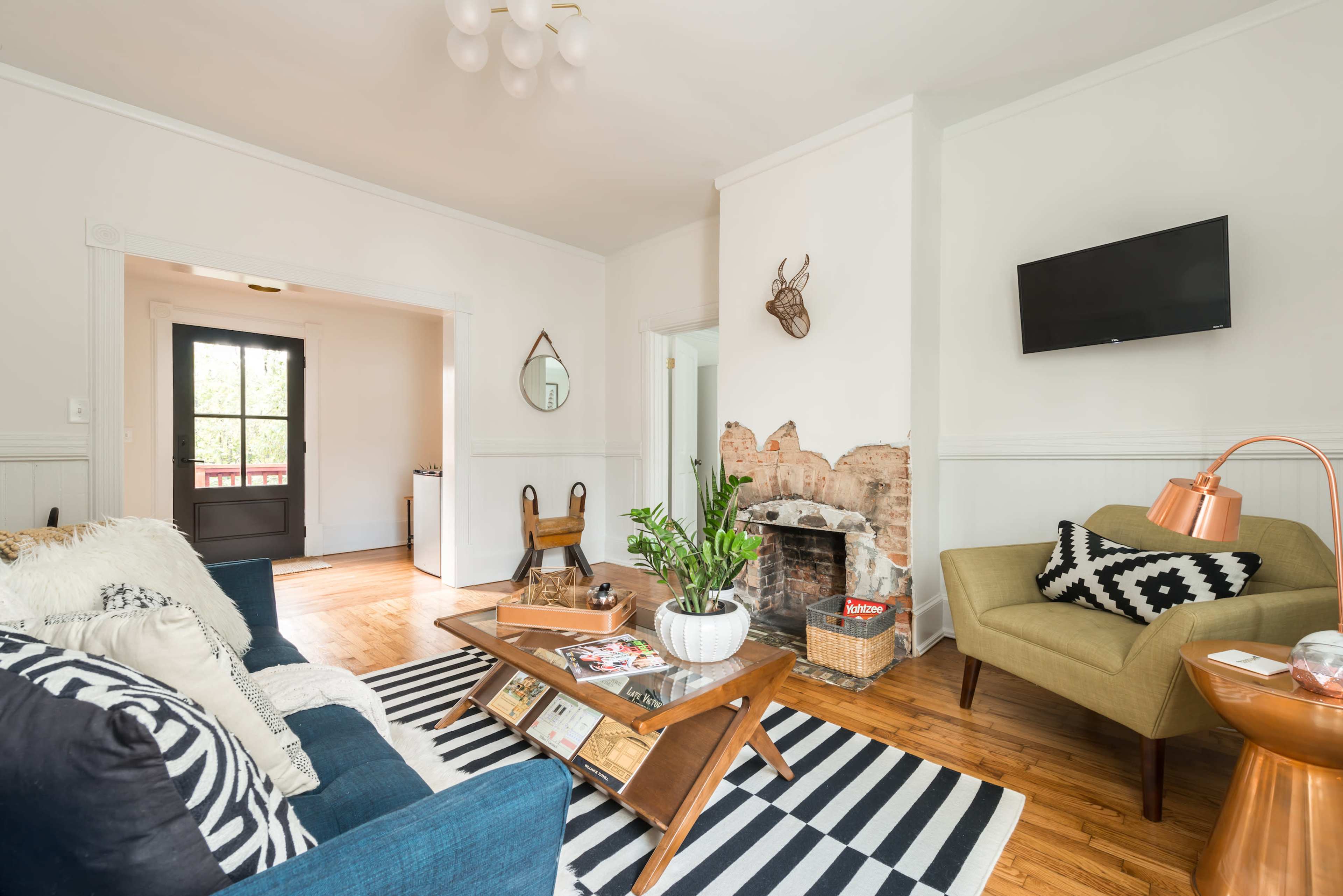 The living room features a blue sofa, a wooden coffee table on a striped rug, a brick fireplace, and a wall-mounted television.