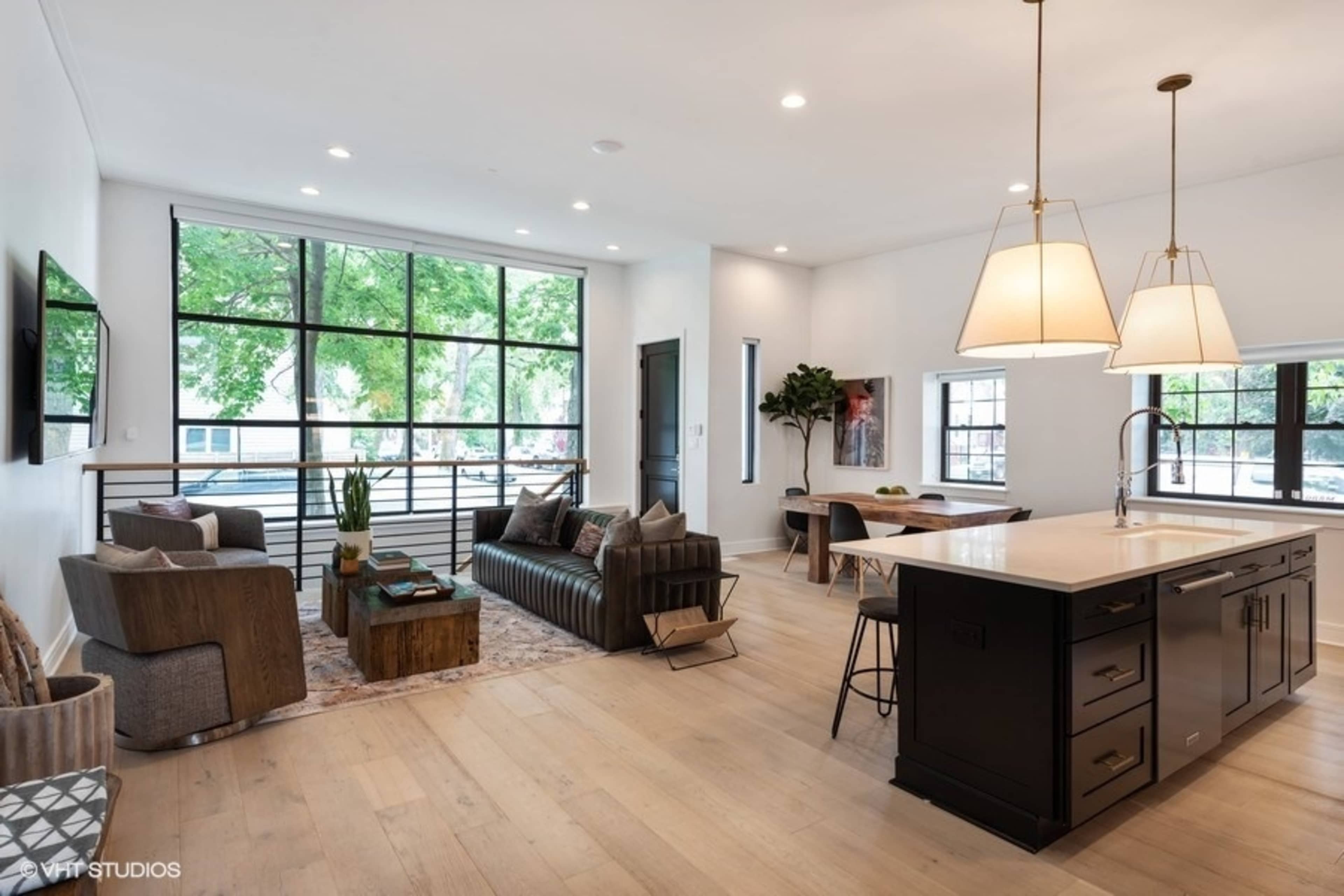 A modern, open-concept living space with a kitchen island, dining area, and large windows letting in natural light.