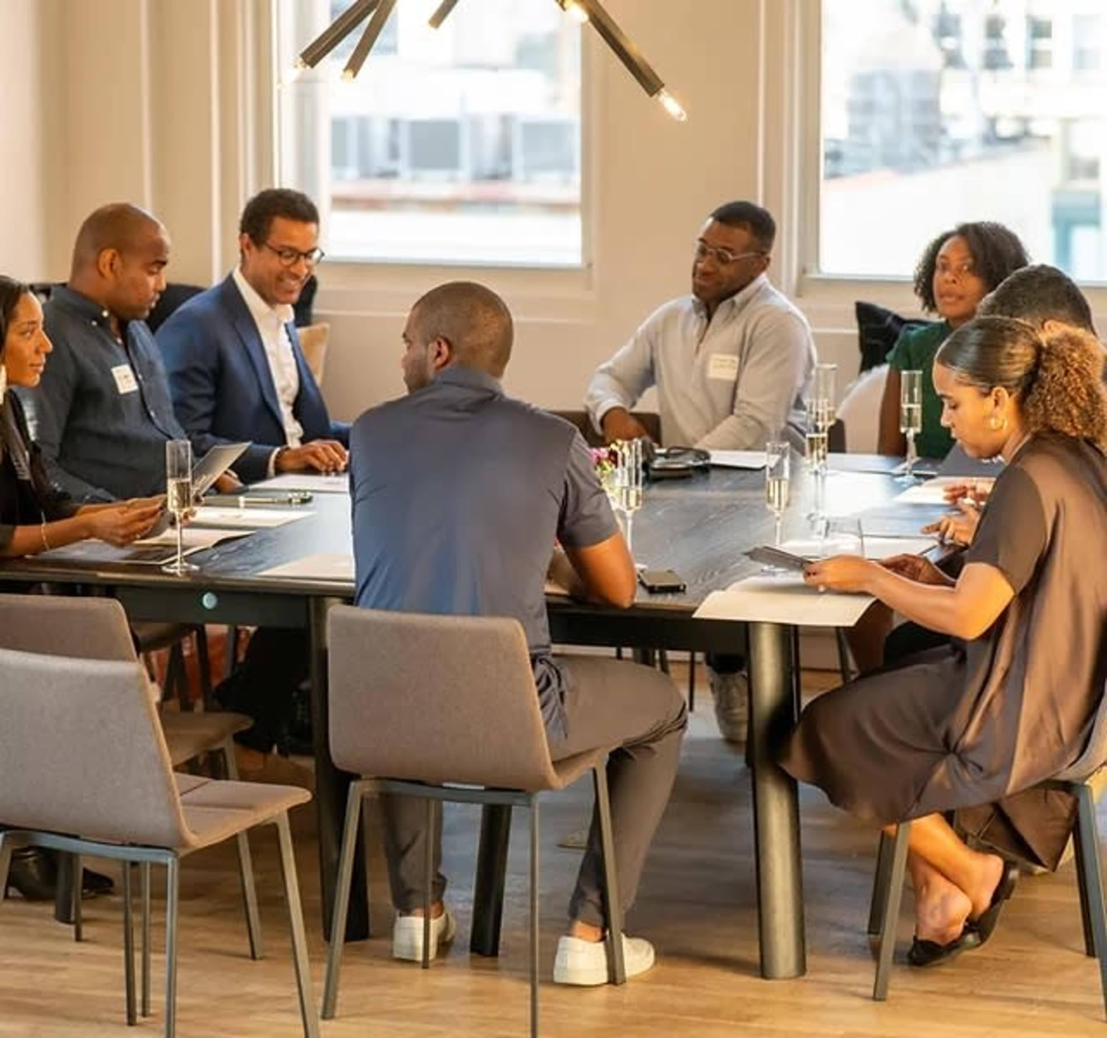 A group of ten people sits around a large conference table in a modern meeting room, engaging in discussion and reviewing materials.