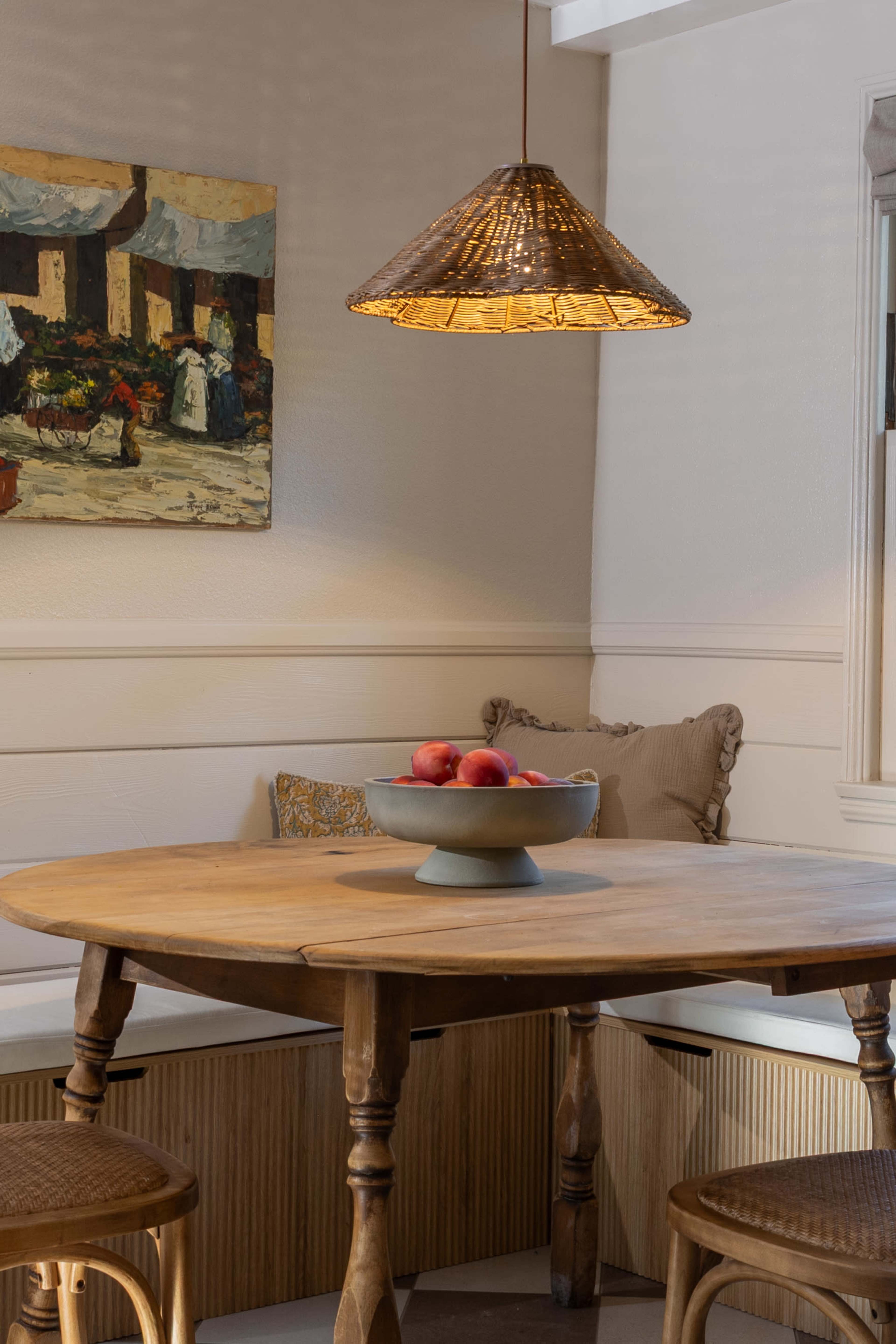 The image shows a cozy dining area with a wooden table, a bowl of apples on it, and a pendant light hanging above, next to a wall adorned with a painting.