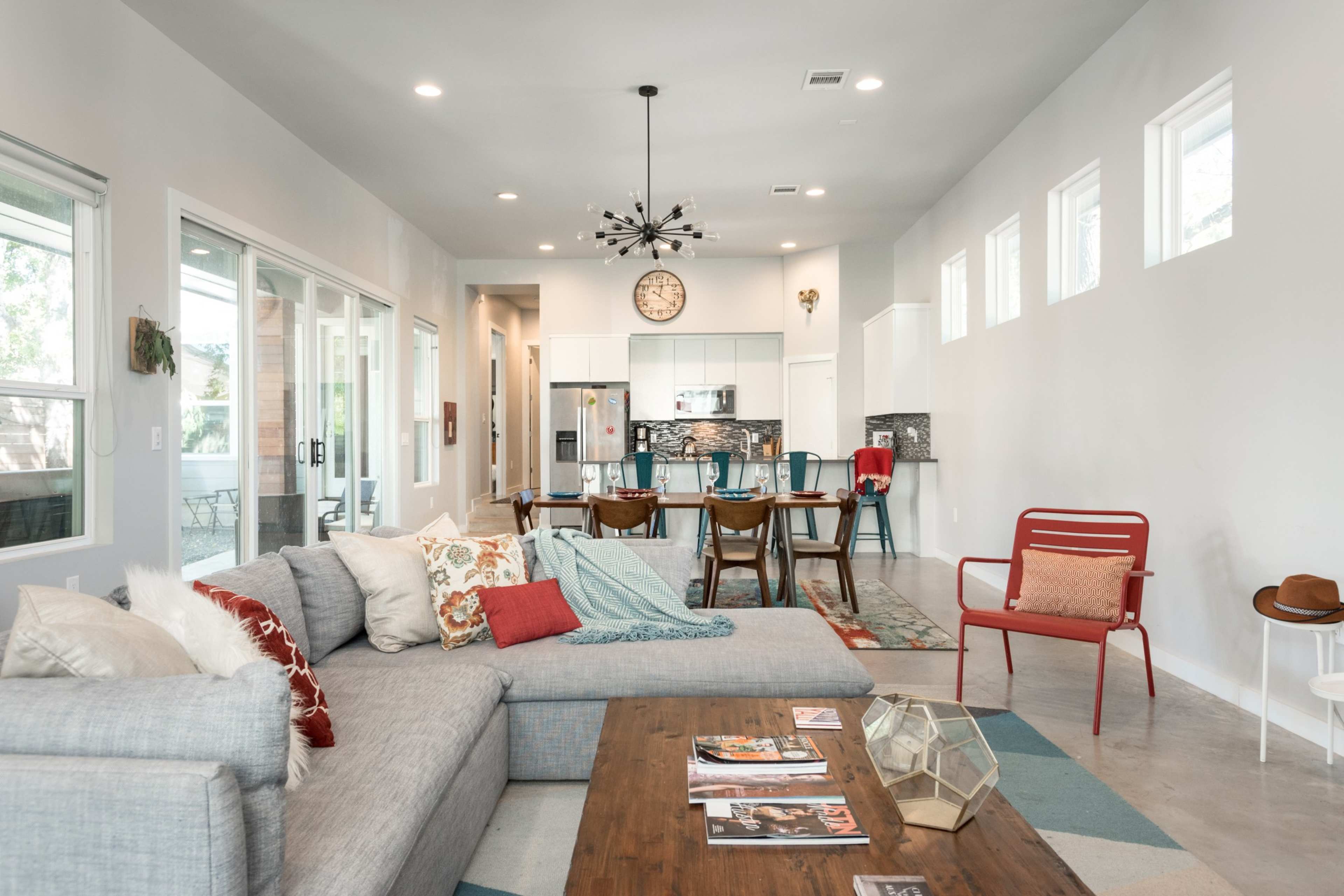 A modern living room with a gray sectional sofa, a wooden coffee table, and a dining area in the background featuring a long table with chairs.