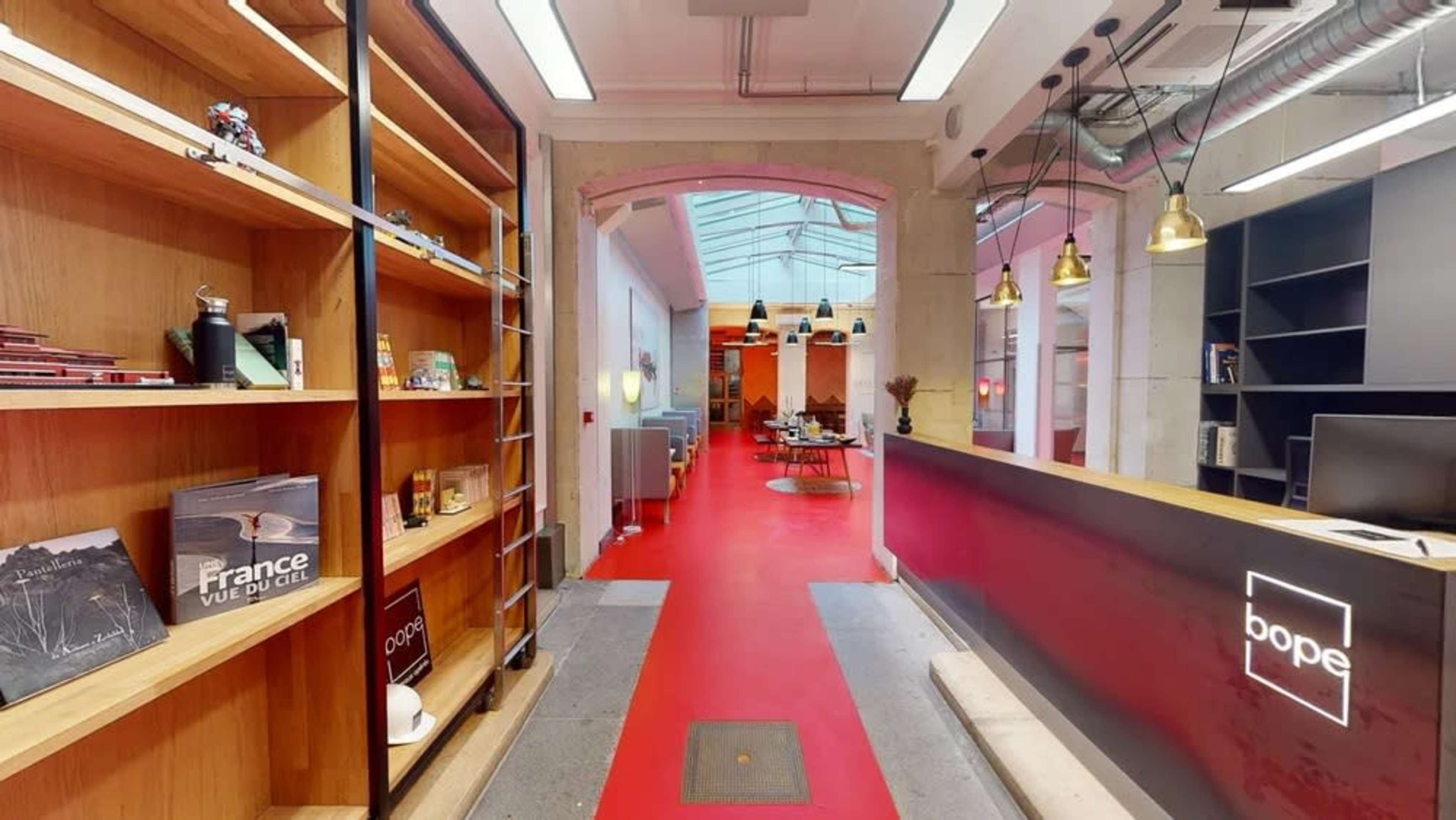 A modern interior with a red carpet, a wooden reception desk on the right, and shelves displaying various items along the left wall.