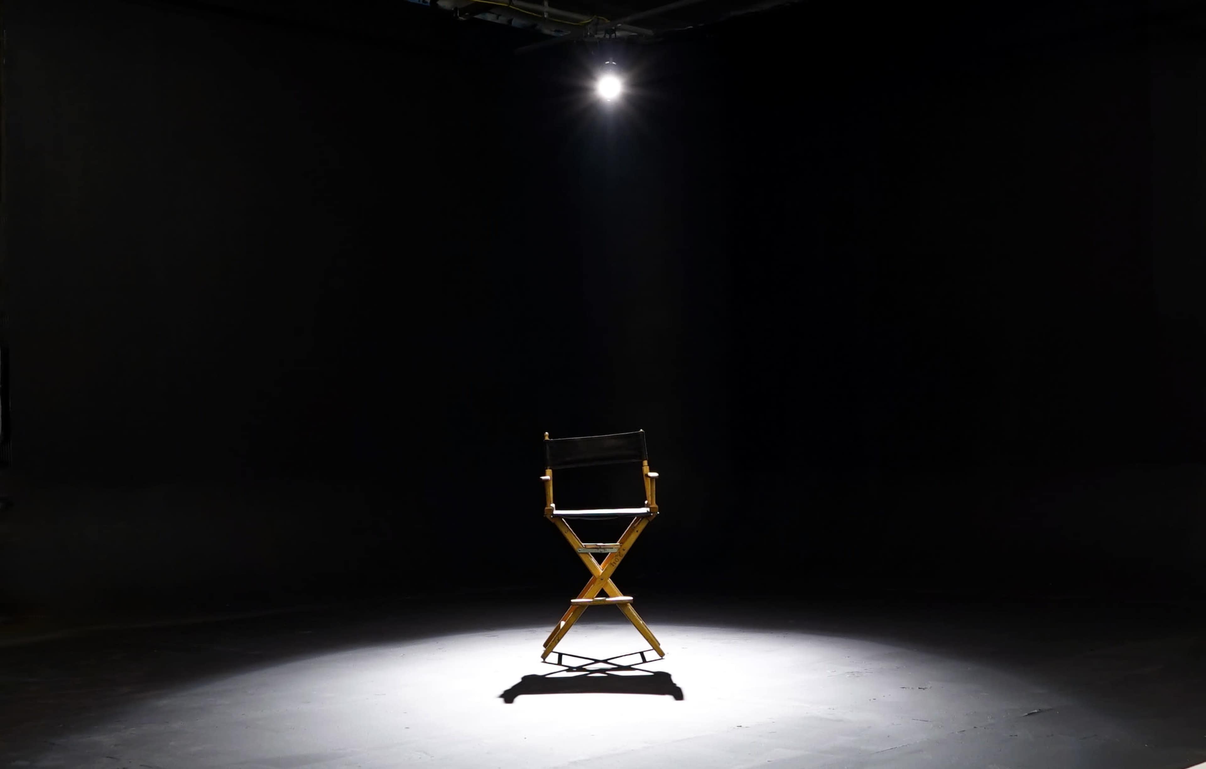 A director's chair stands alone under a single spotlight in a dark room.
