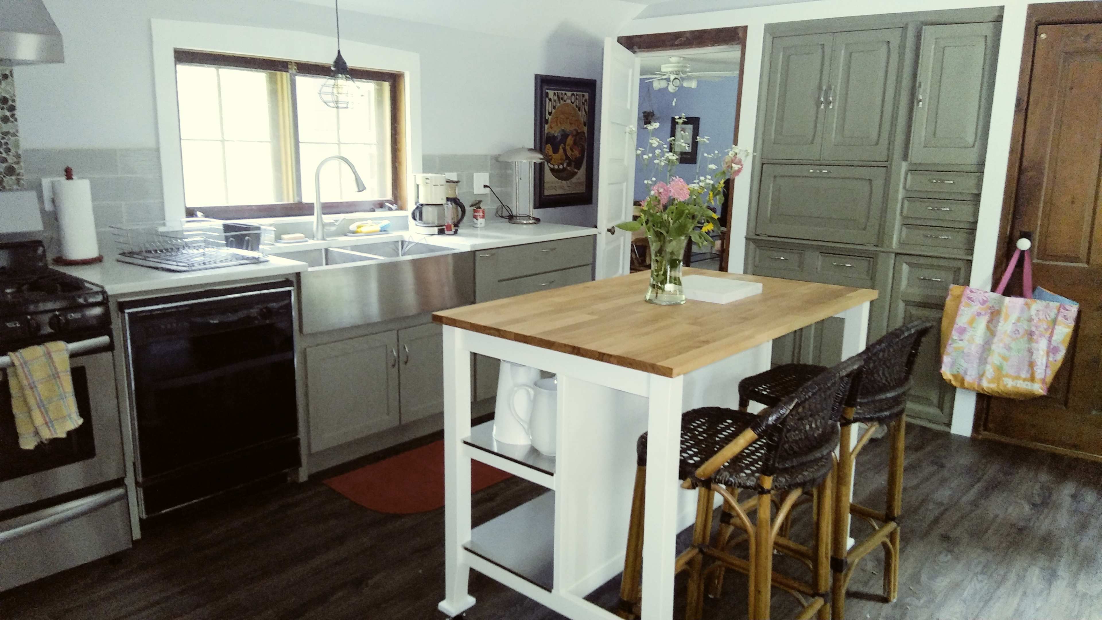 A kitchen with gray cabinets, a stainless steel sink, a wooden island with bar stools, and a vase of flowers on the counter.