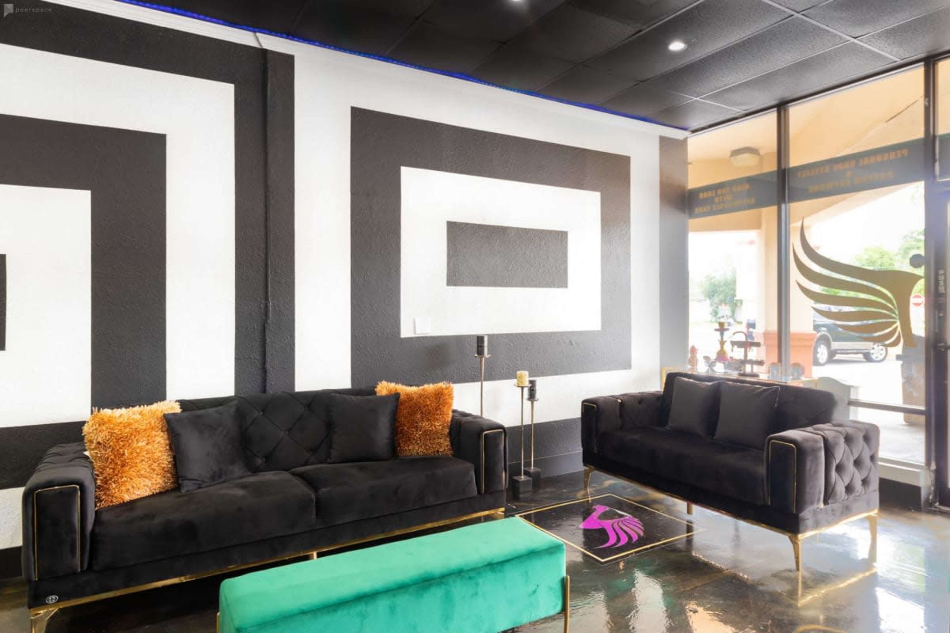 A modern lounge area with two black sofas, a green ottoman, and a geometric wall design featuring bold black and white shapes.