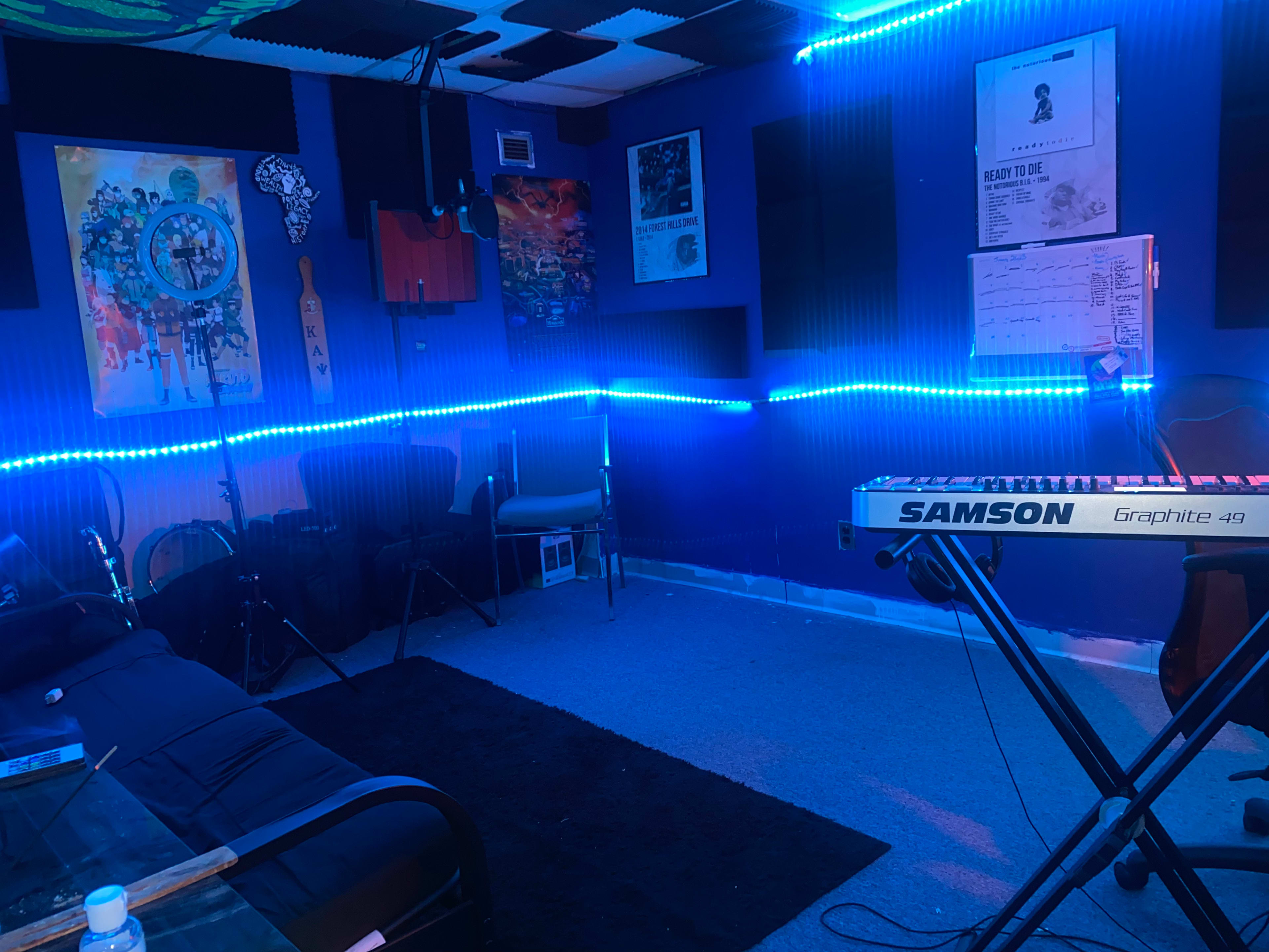 A music studio with blue LED lights, a keyboard, a seating area, and various art pieces on the walls.