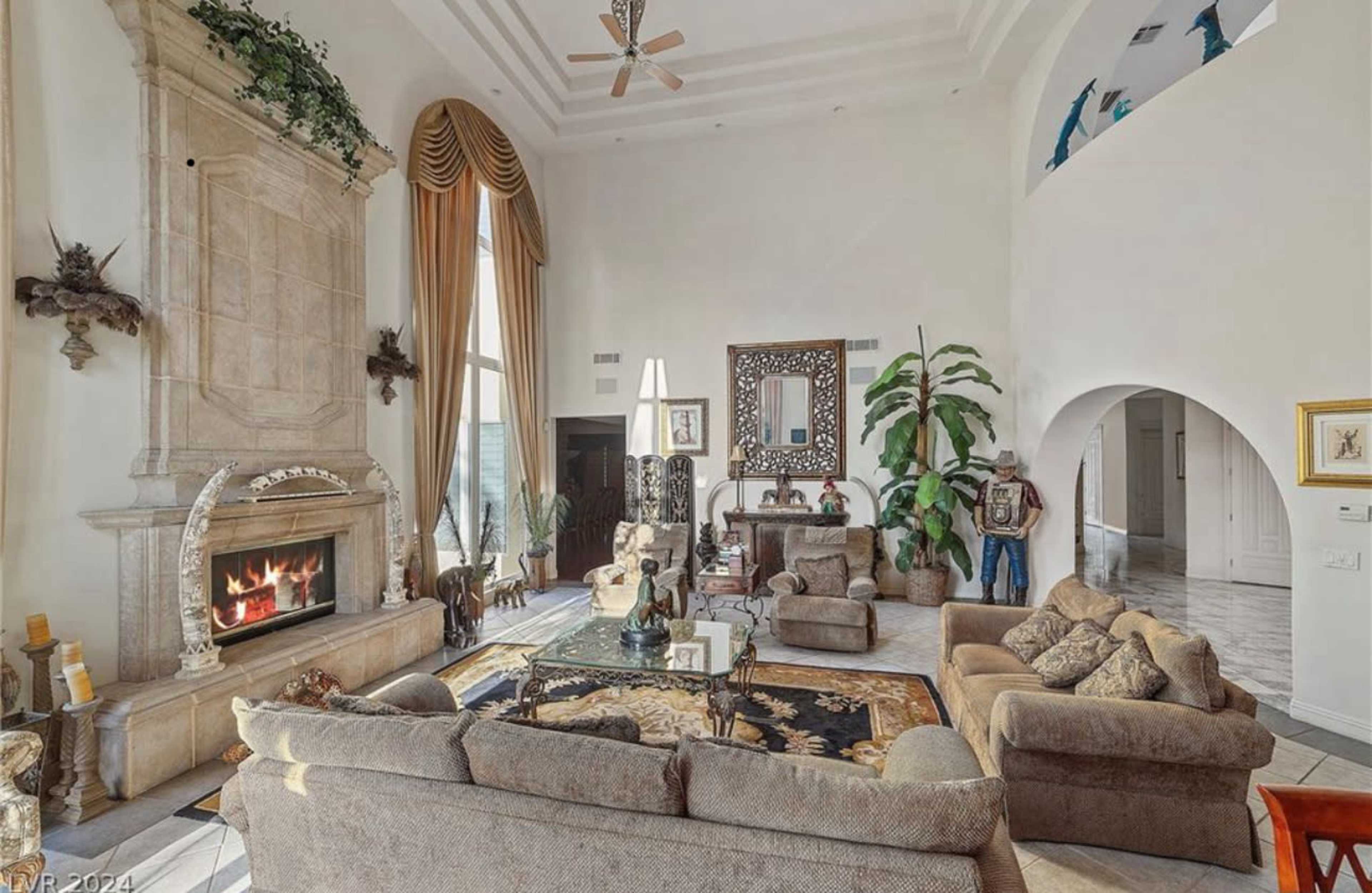 A spacious living room with a large fireplace, plush seating, and tall windows letting in natural light.