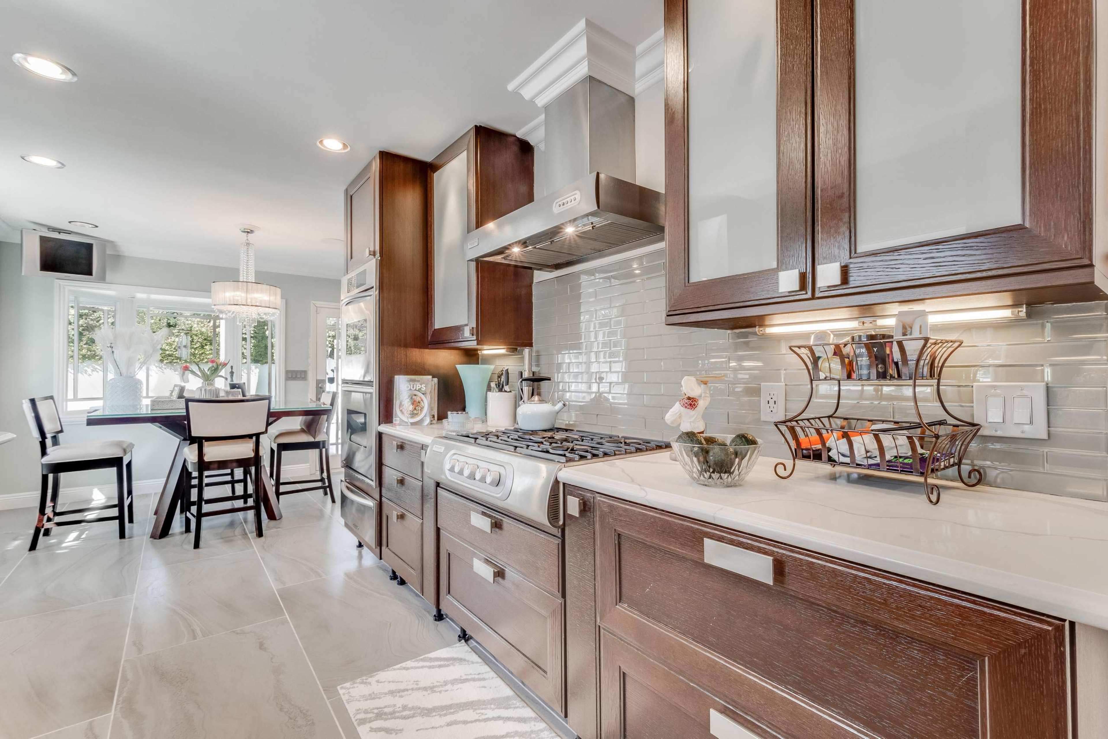 A modern kitchen with dark wooden cabinets, stainless steel appliances, and a large countertop, leading into a dining area with a table and chairs.