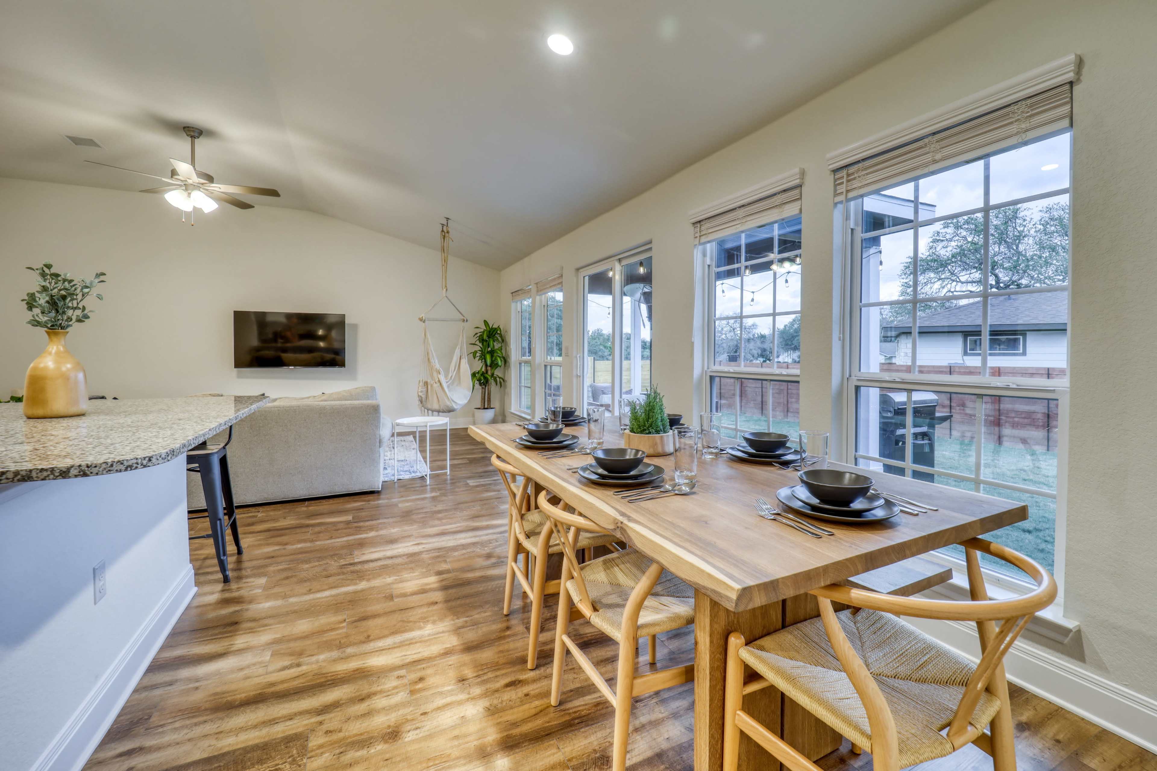 A spacious dining area with a wooden table set for six, alongside a modern living space featuring a sofa and a TV.