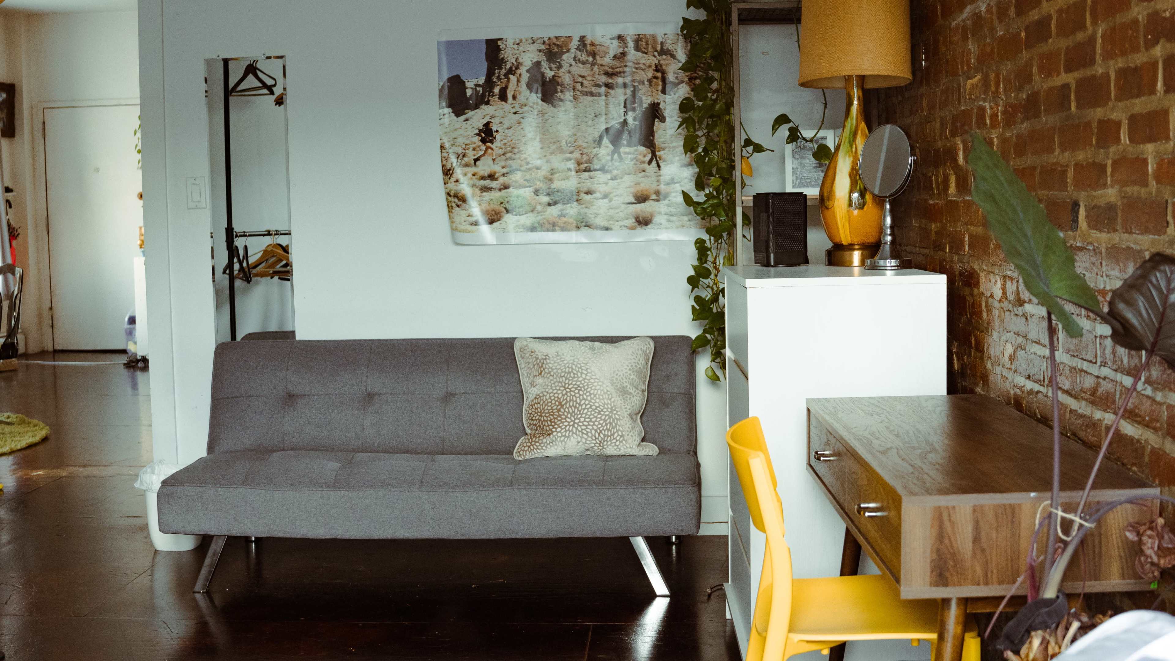 A living space with a gray sofa, a yellow chair, a wooden desk, and a large photo on the wall above a white cabinet.