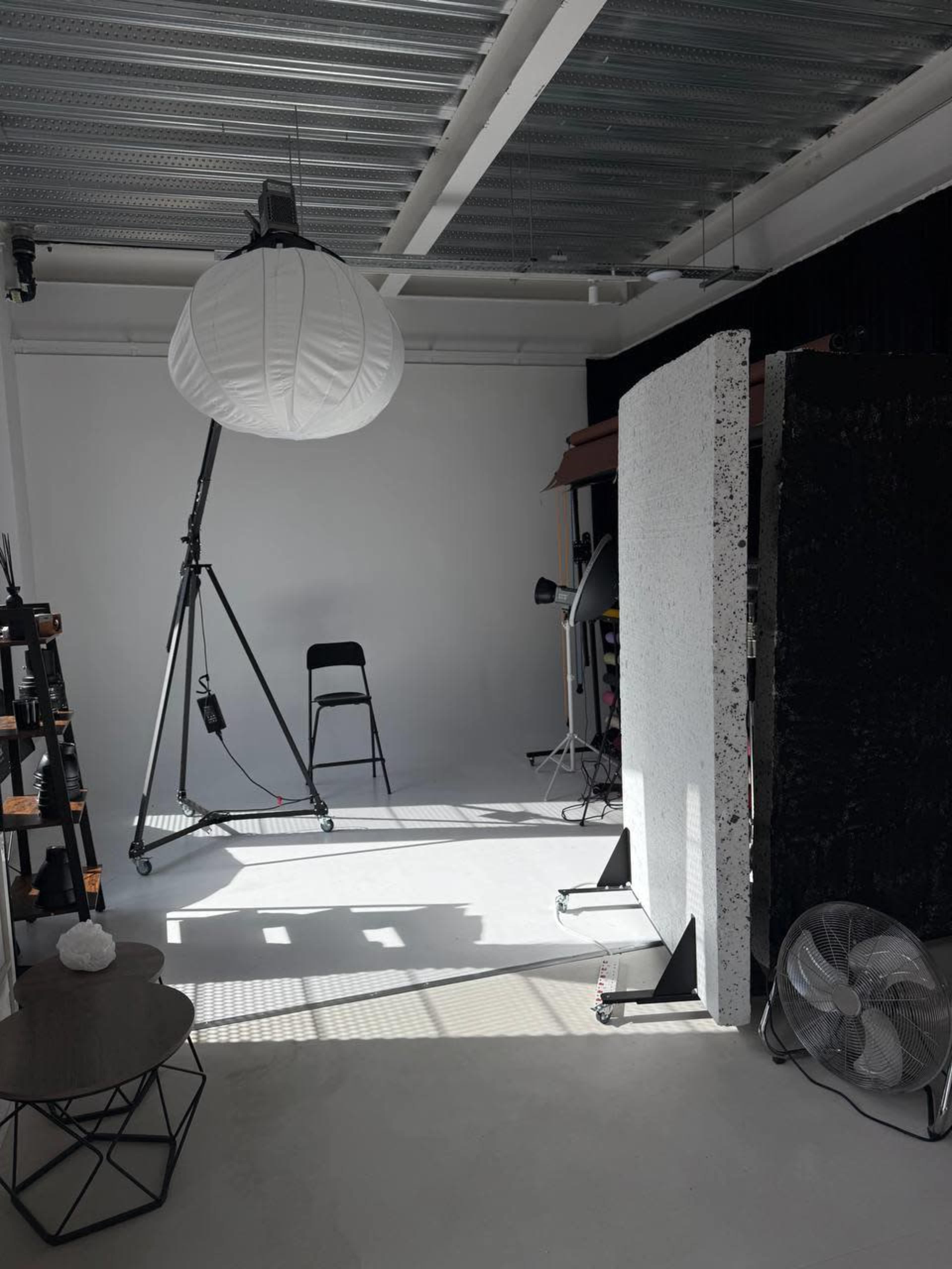 The image shows a photography studio with a backdrop, a chair, and various equipment, including a large light fixture and a fan.